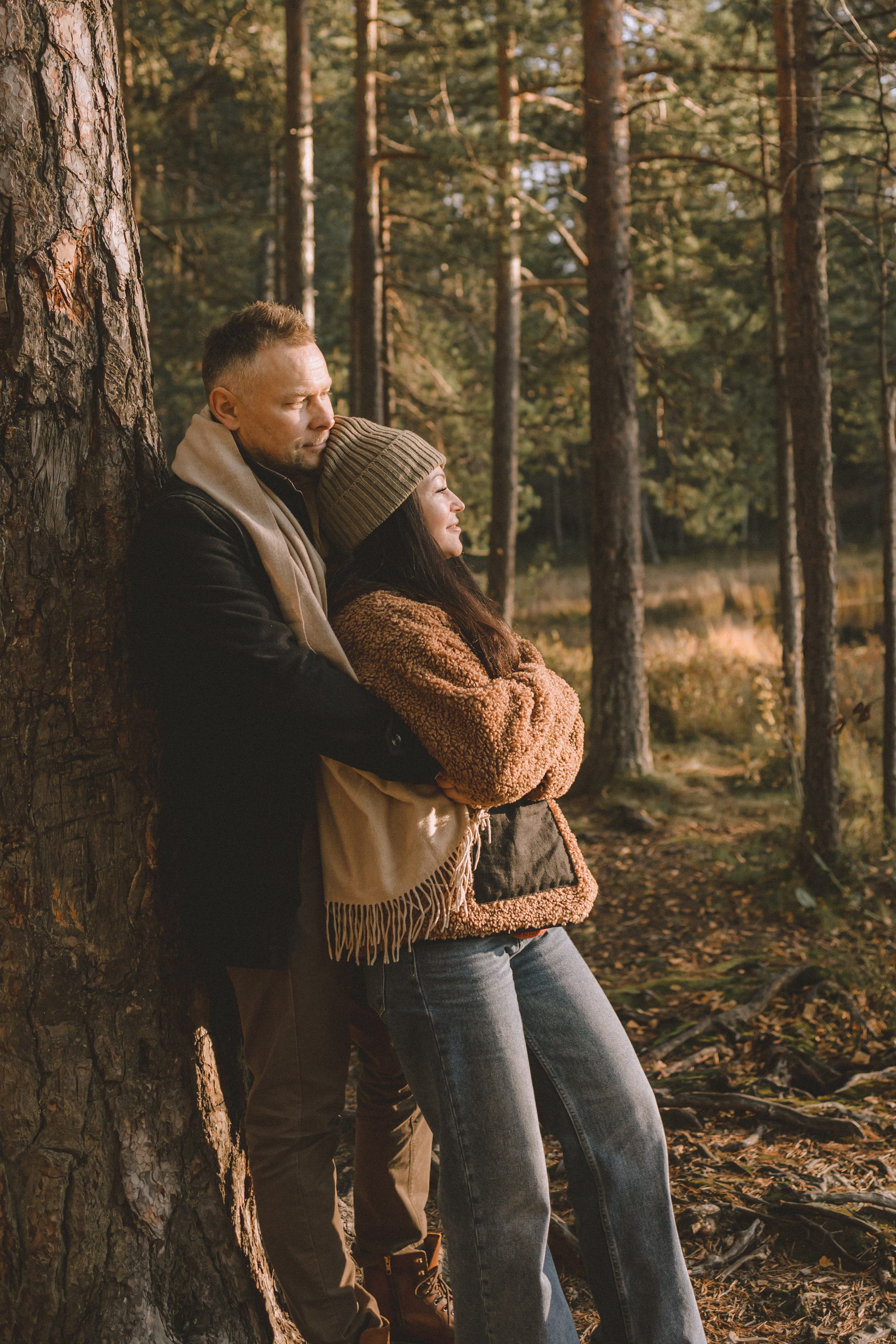 муж обнимает жену они стоят у дерева и любуются осенним лесом