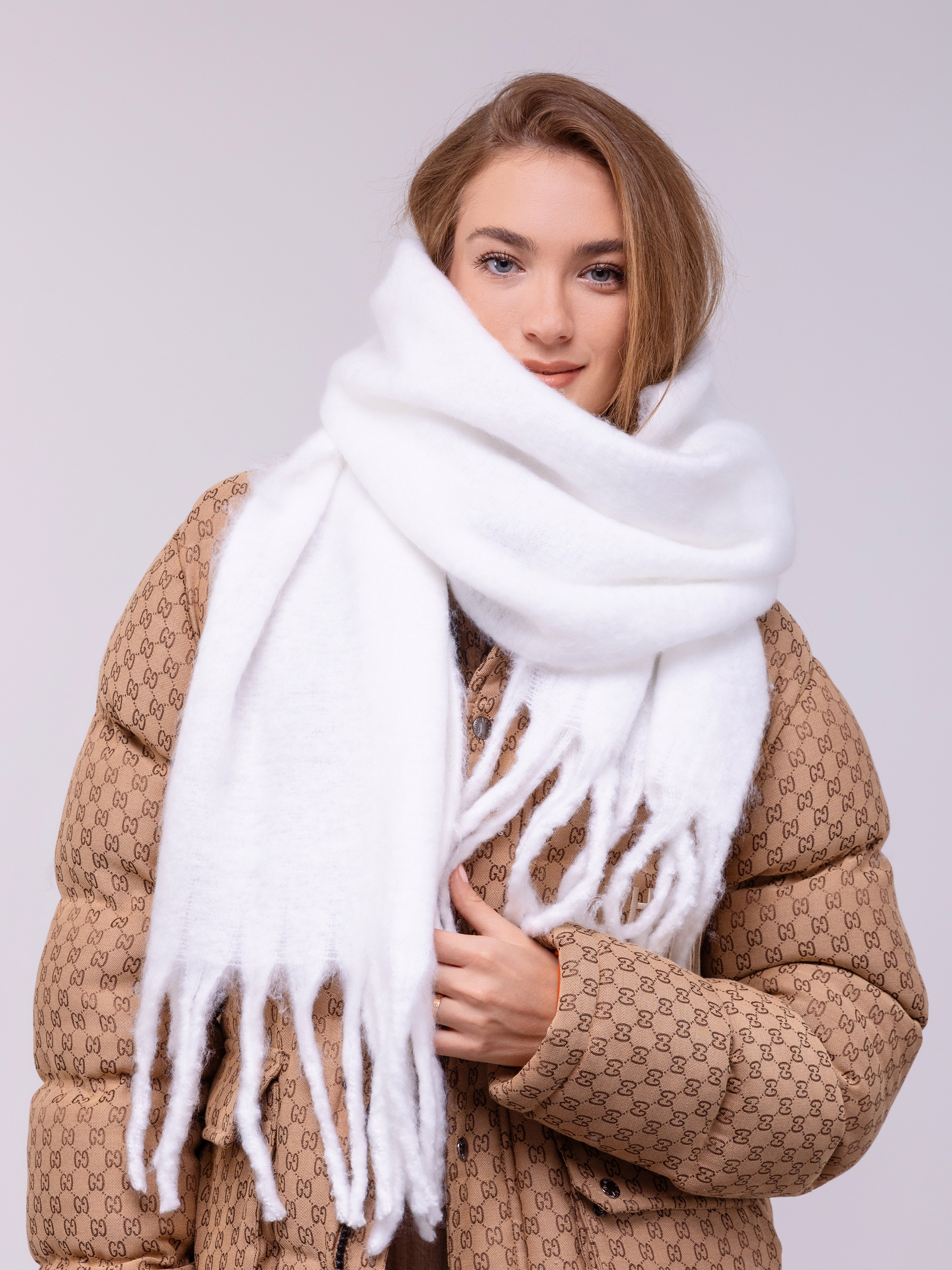 Белый палантин с длинными кистями обвязан вокруг шеи девушки.