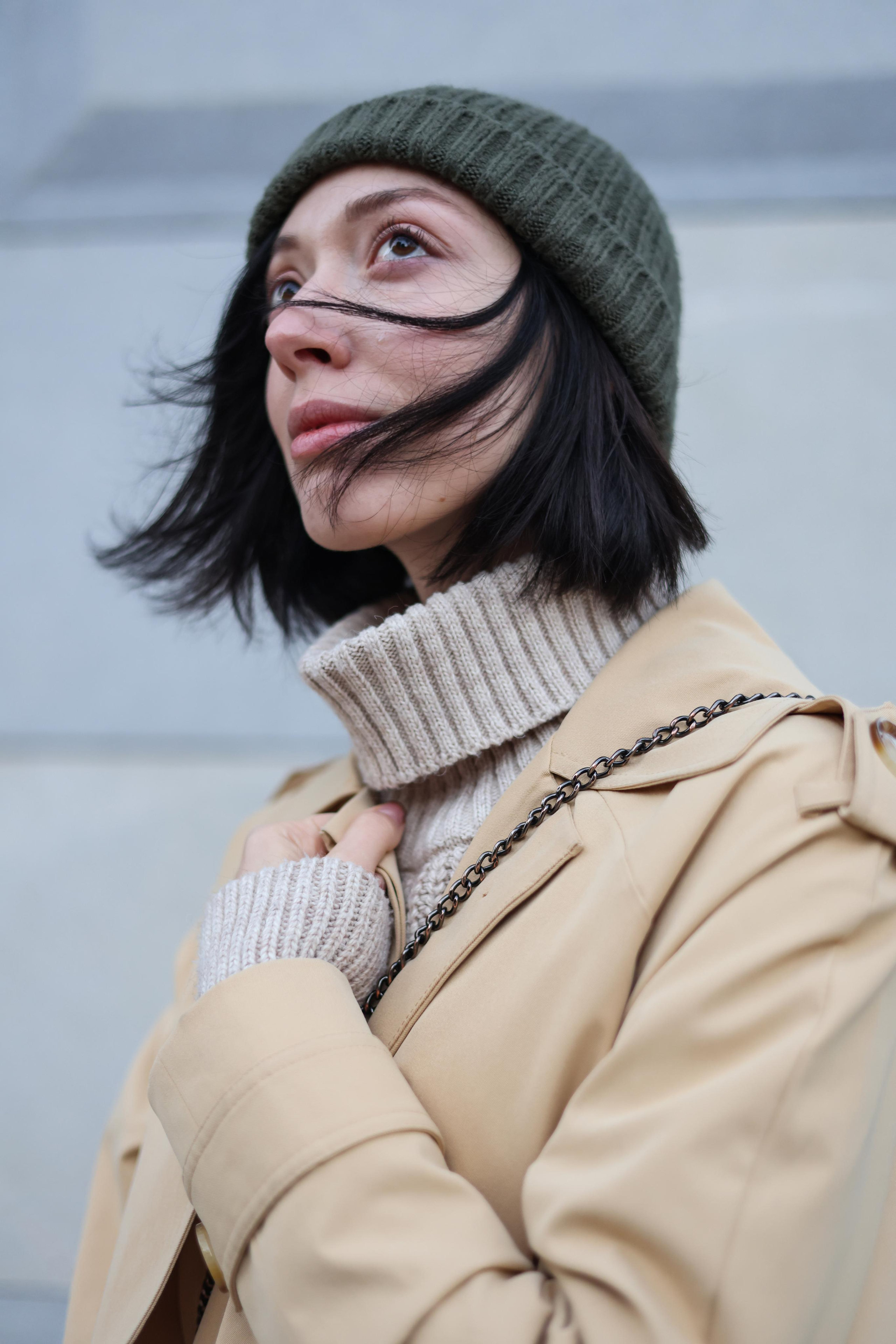 Девушка Наталья Штин в шапке, пальто и водолазке на улице. Волосы развиваются на ветру