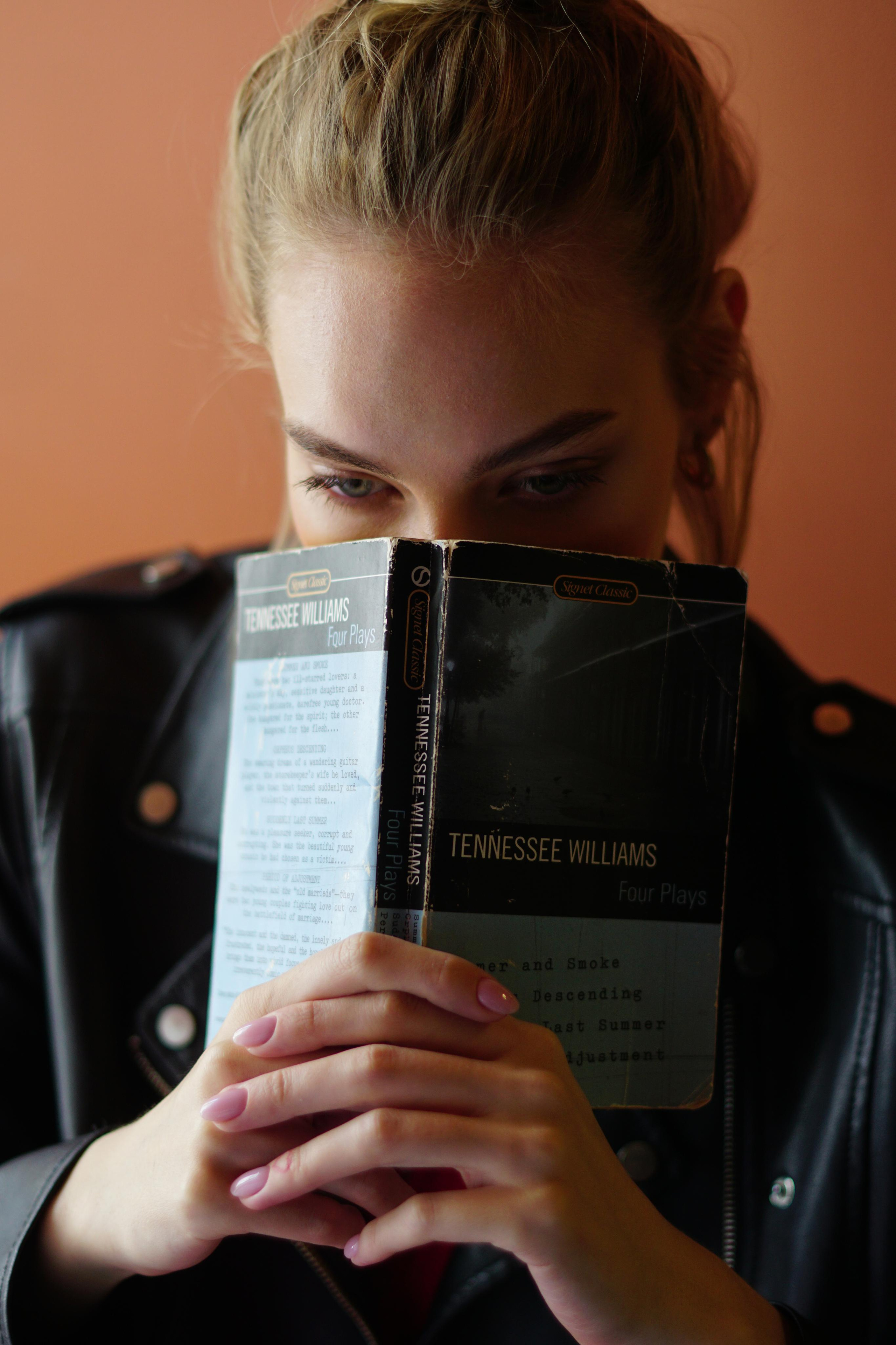 Девушка прикрывает лицо книгой Tennesse Williams 