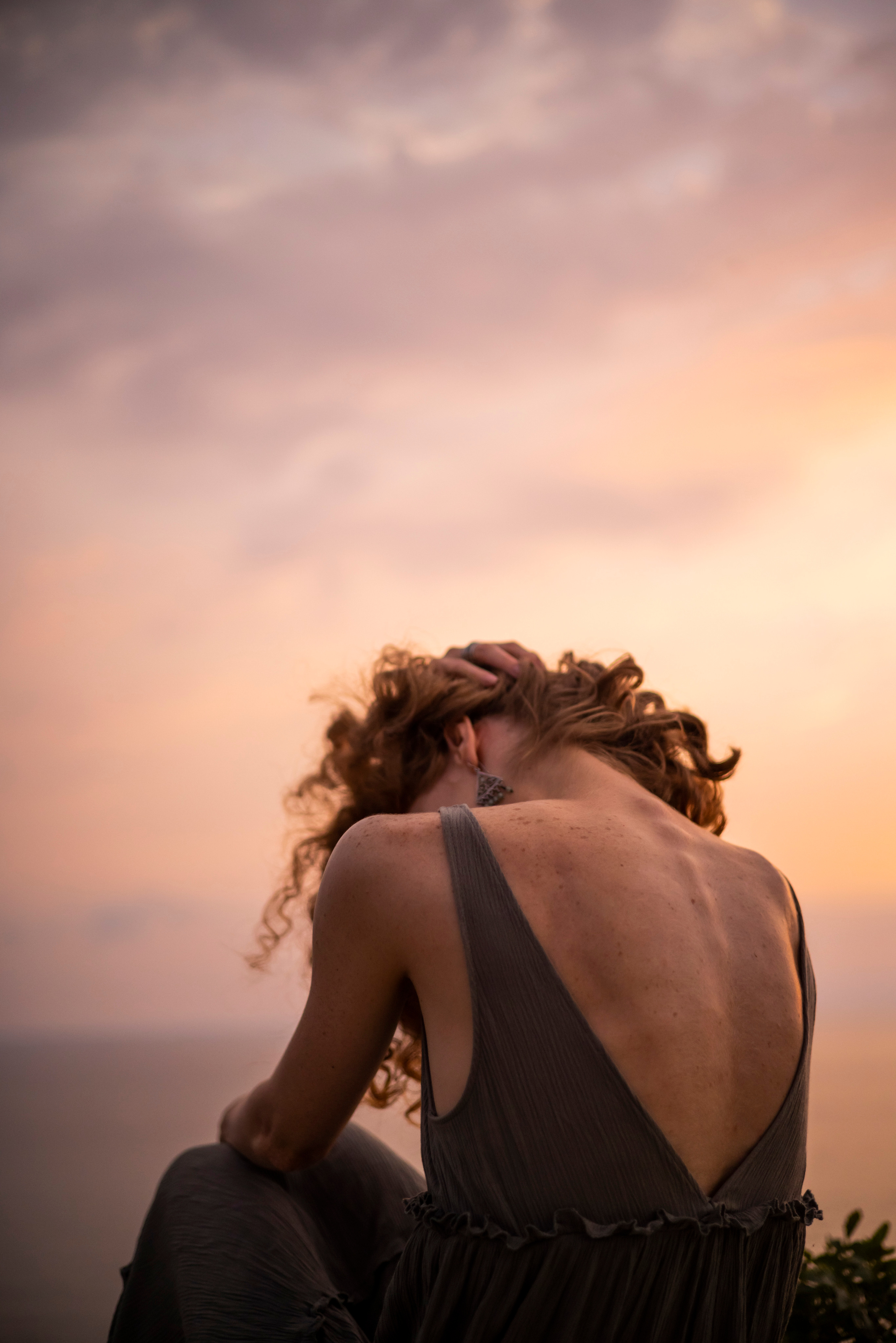 Девушка сидит на холме спиной во время заката