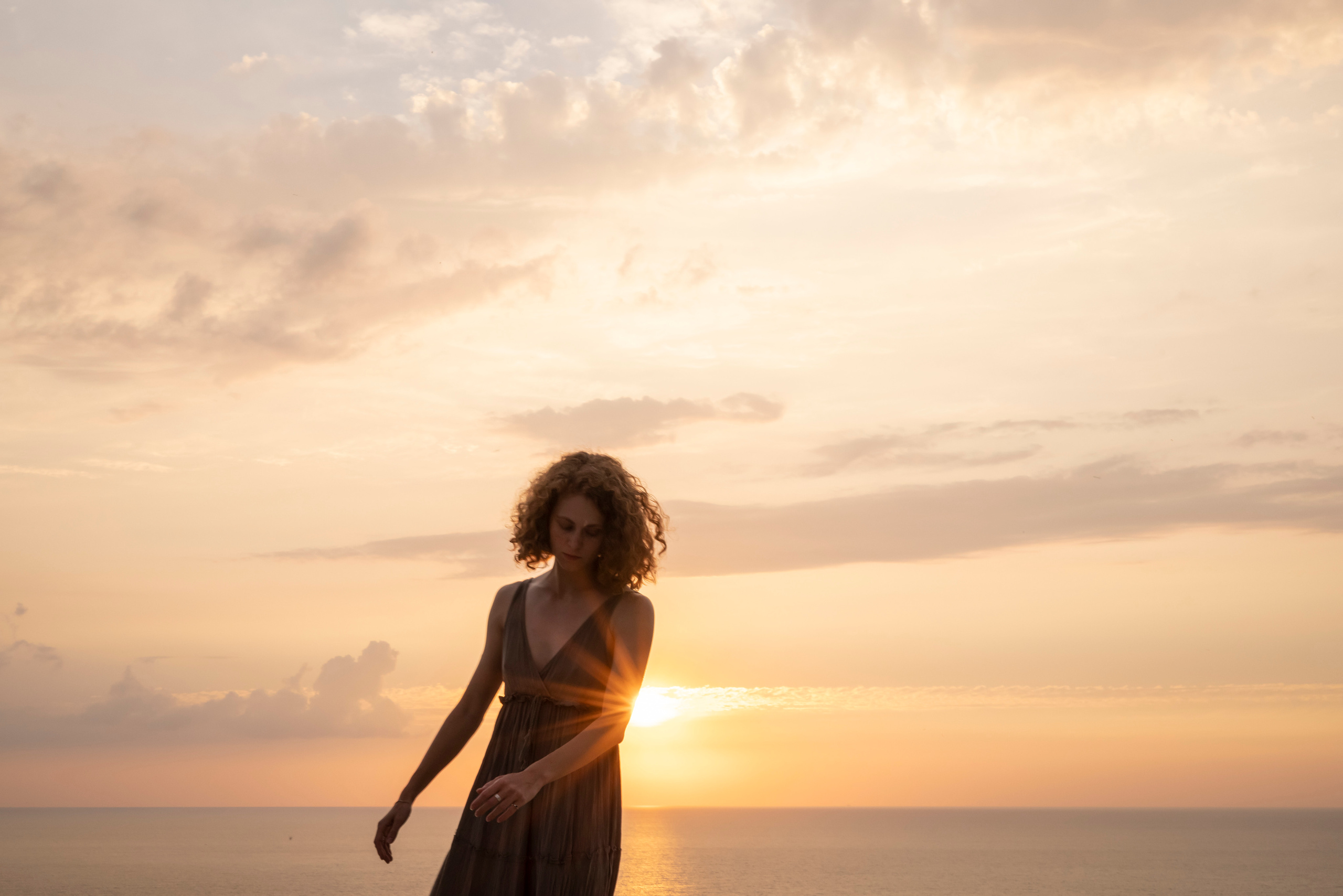 Девушка на море склонила голову на фоне заката