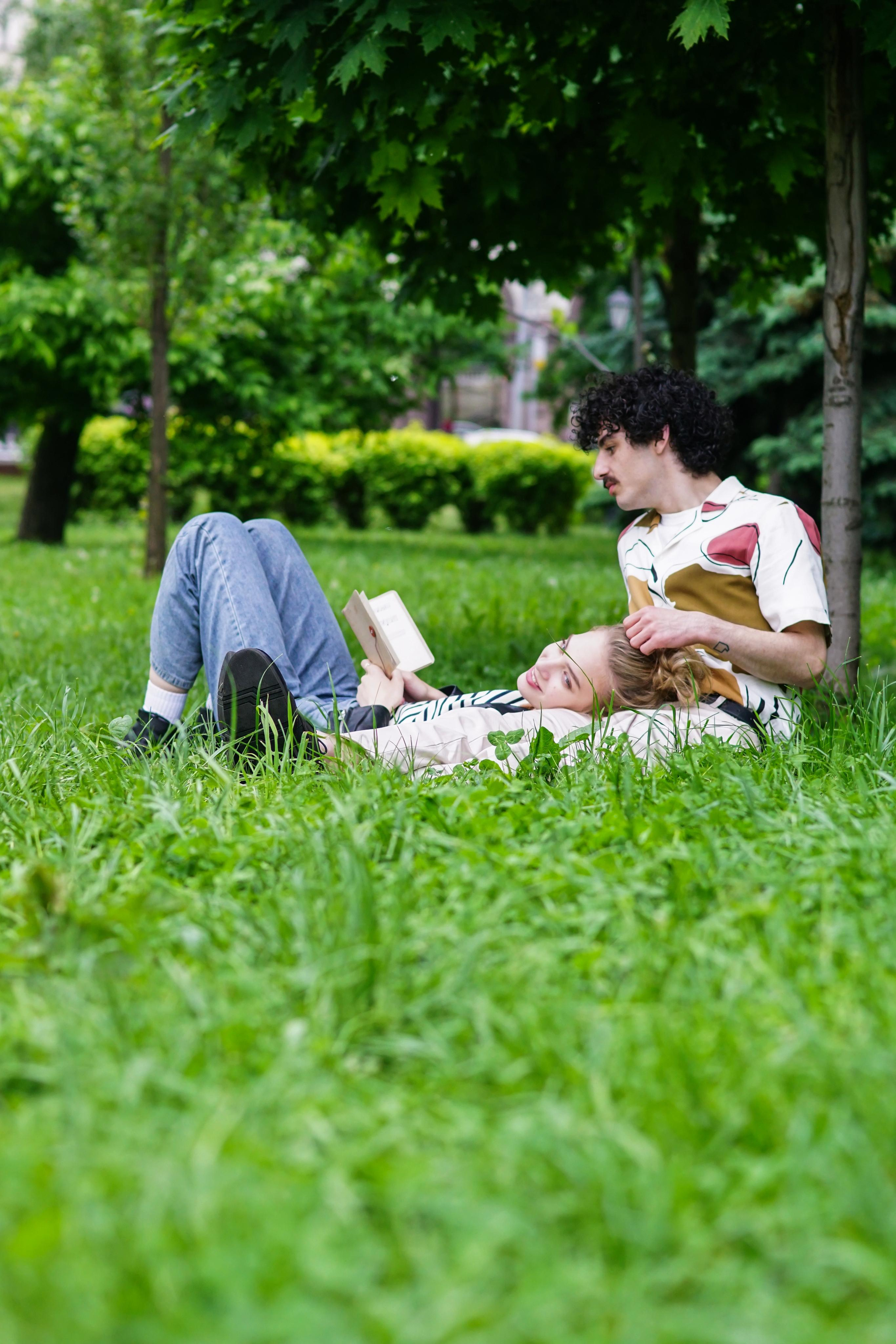 Пара в парке на траве, где девушка лежит на коленях у мужчины