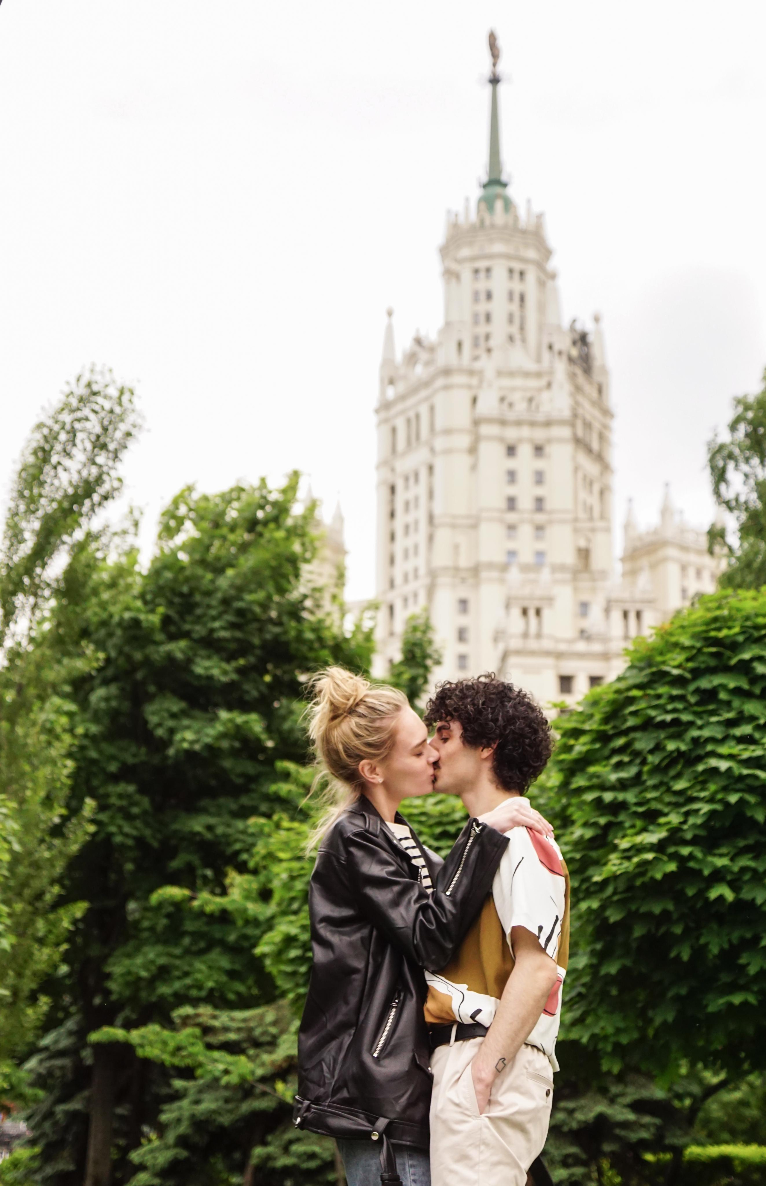 Поцелуй мужчины и женщины в парке на фоне высотки