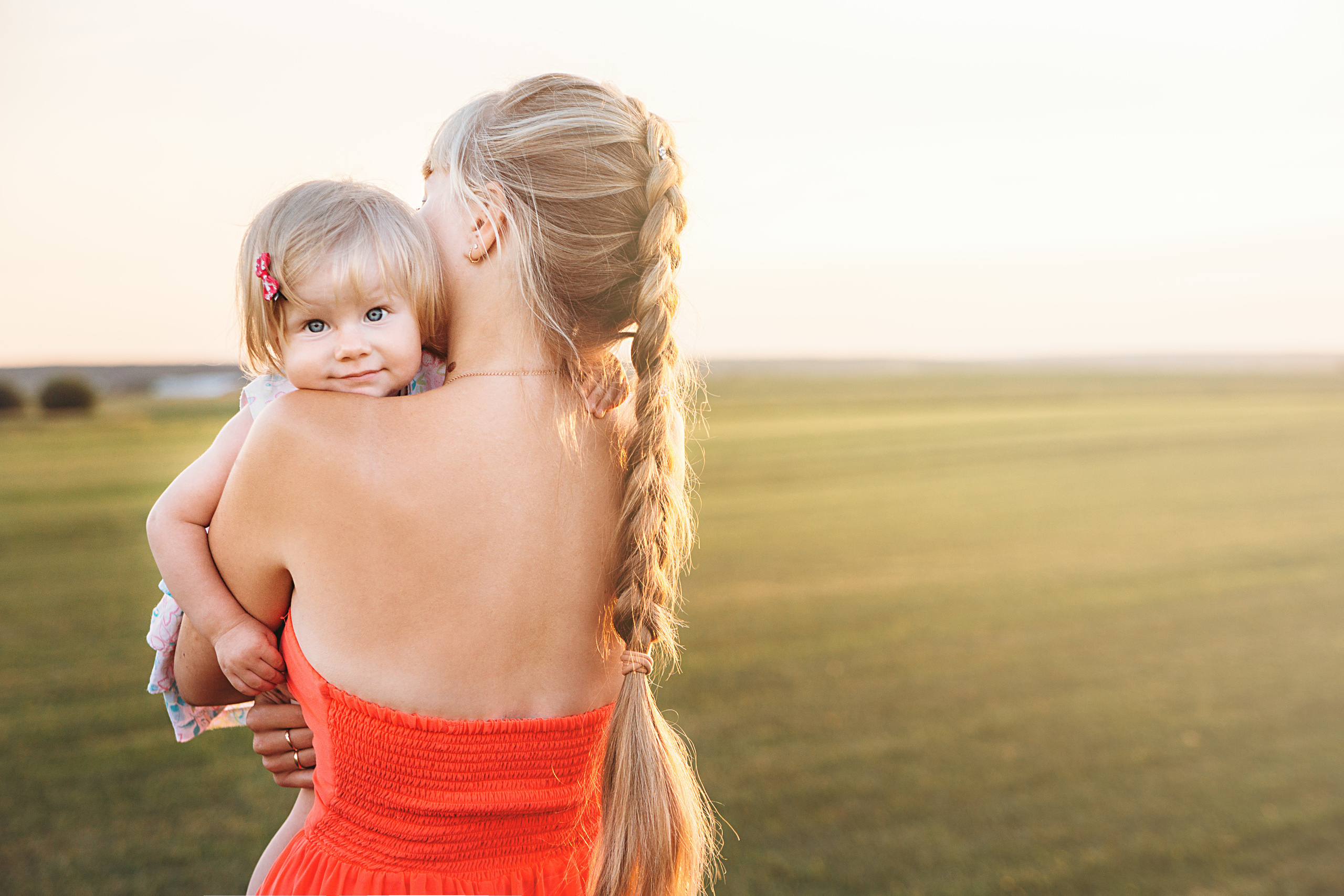 Девочка сидит на руках у мамы на закате, в поле
