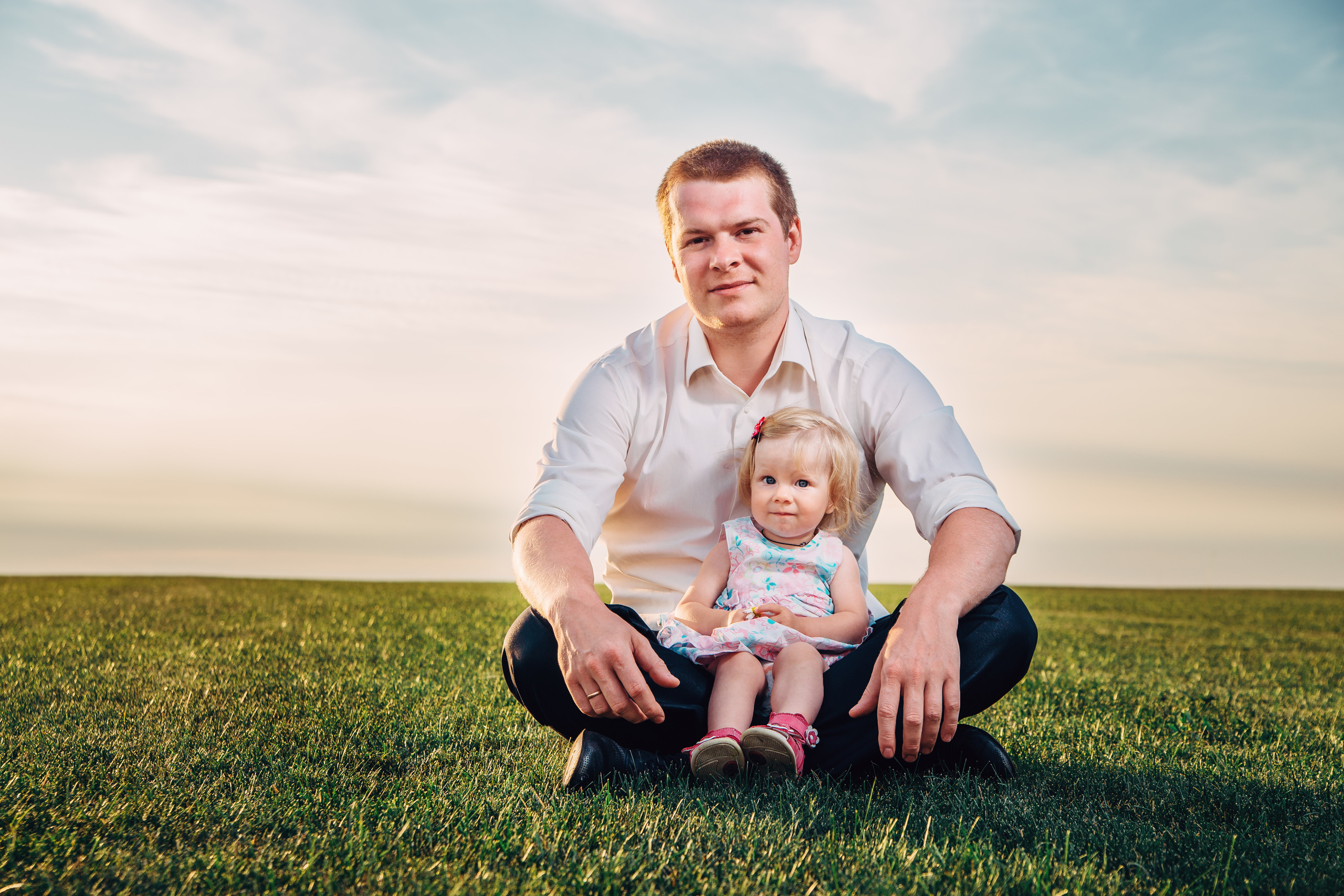 Папа с девочкой сидят в поле на закате, голубое небо с облаками