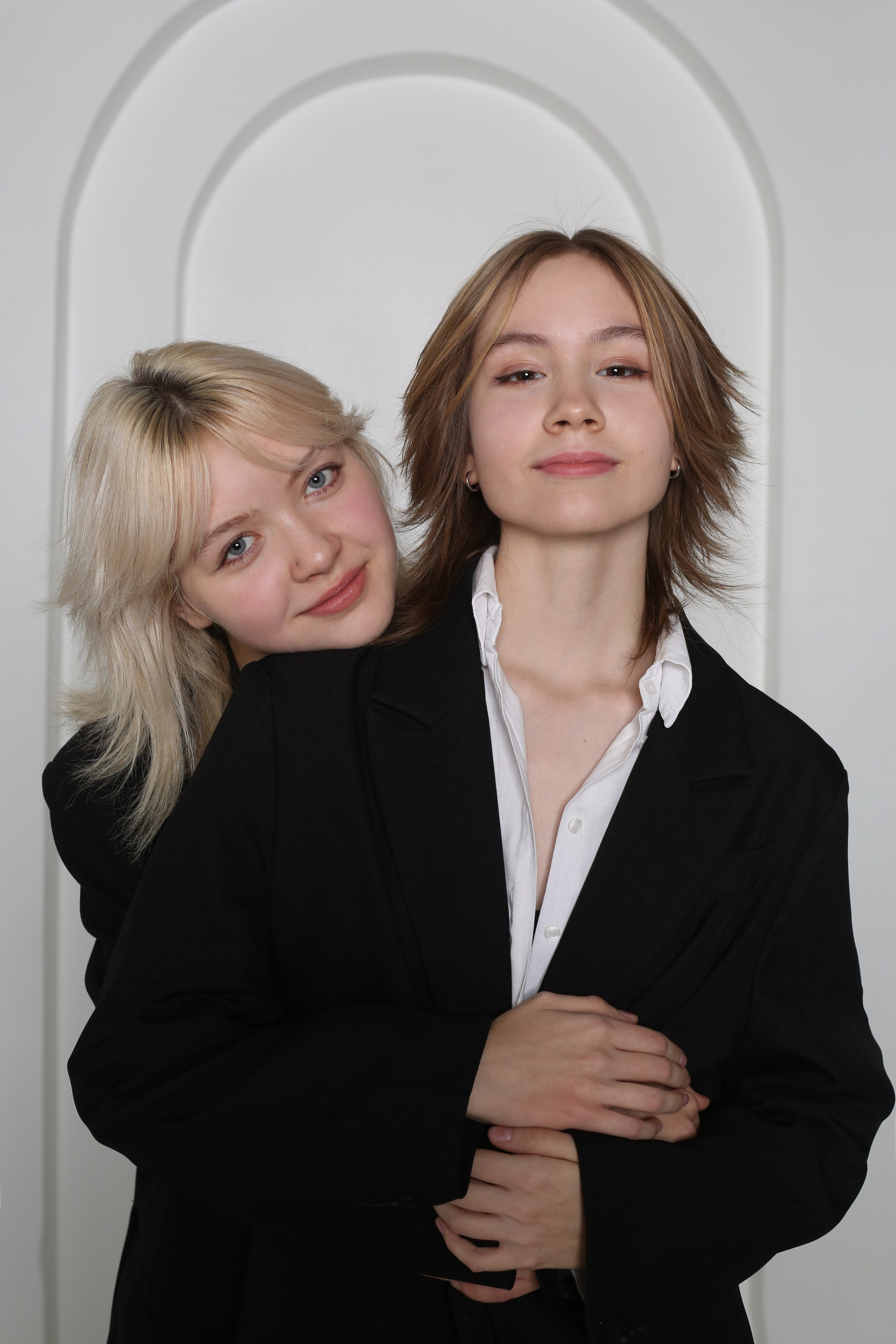 Портрет из фотосессии «Геометрия»: две девушки в черных костюмах обнимаются на белом фоне