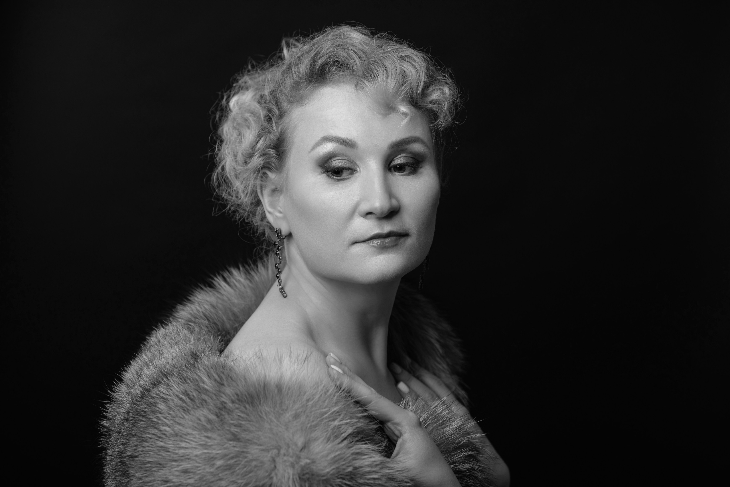 Девушка задумчиво смотрит на свое плечо одетая в меховое манто