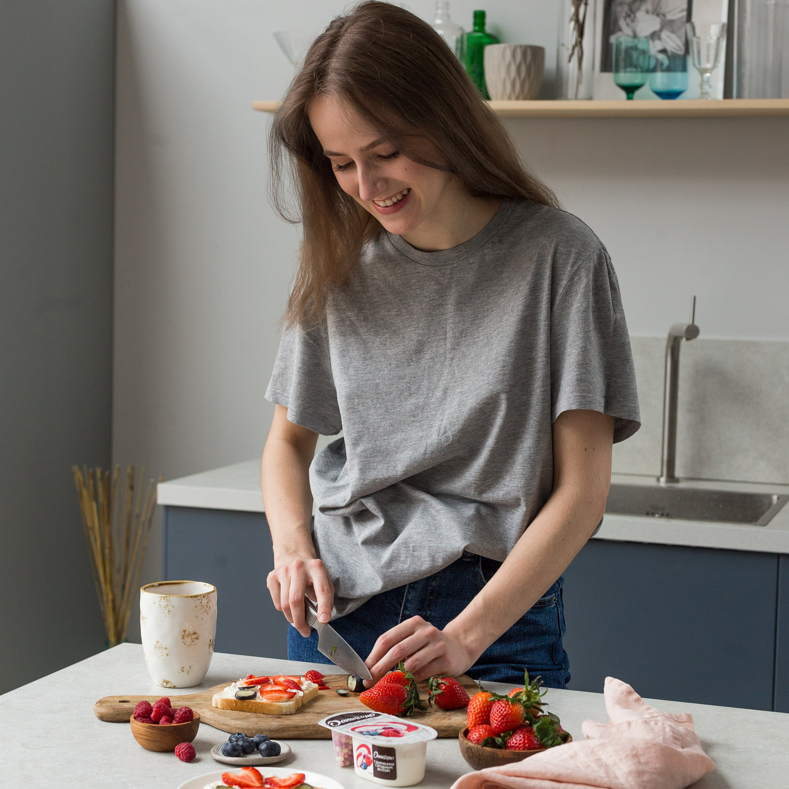 Веселая девушка нарезает клубнику на кухне.