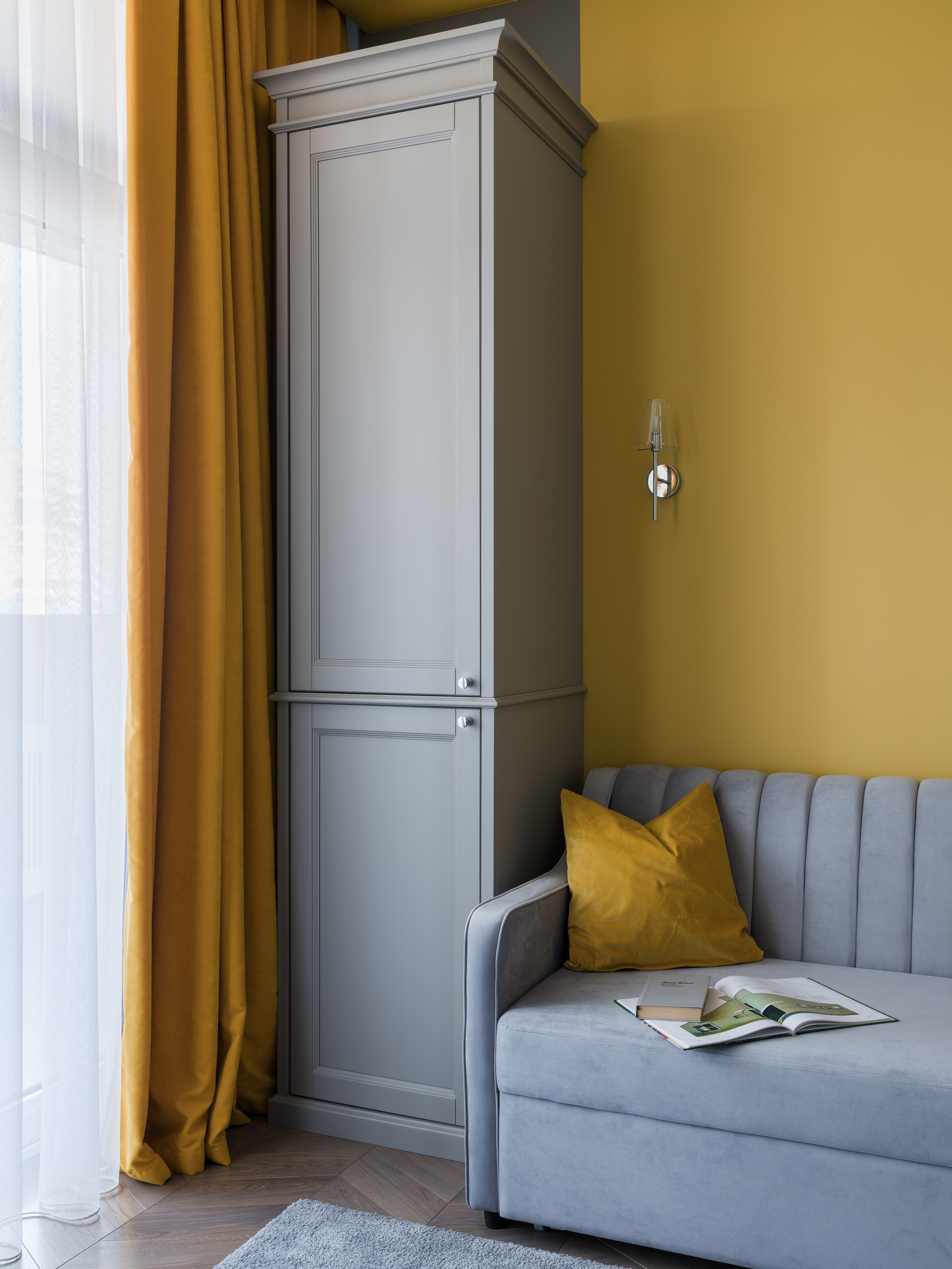 Современный интерьер с серым шкафом в классическом стиле, мягким диваном и акцентами в жёлтом цвете, текстильные детали и спокойная атмосфера; дизайн Евгении Княжевой, интерьерная фотосъёмка Сергей Денисенко.