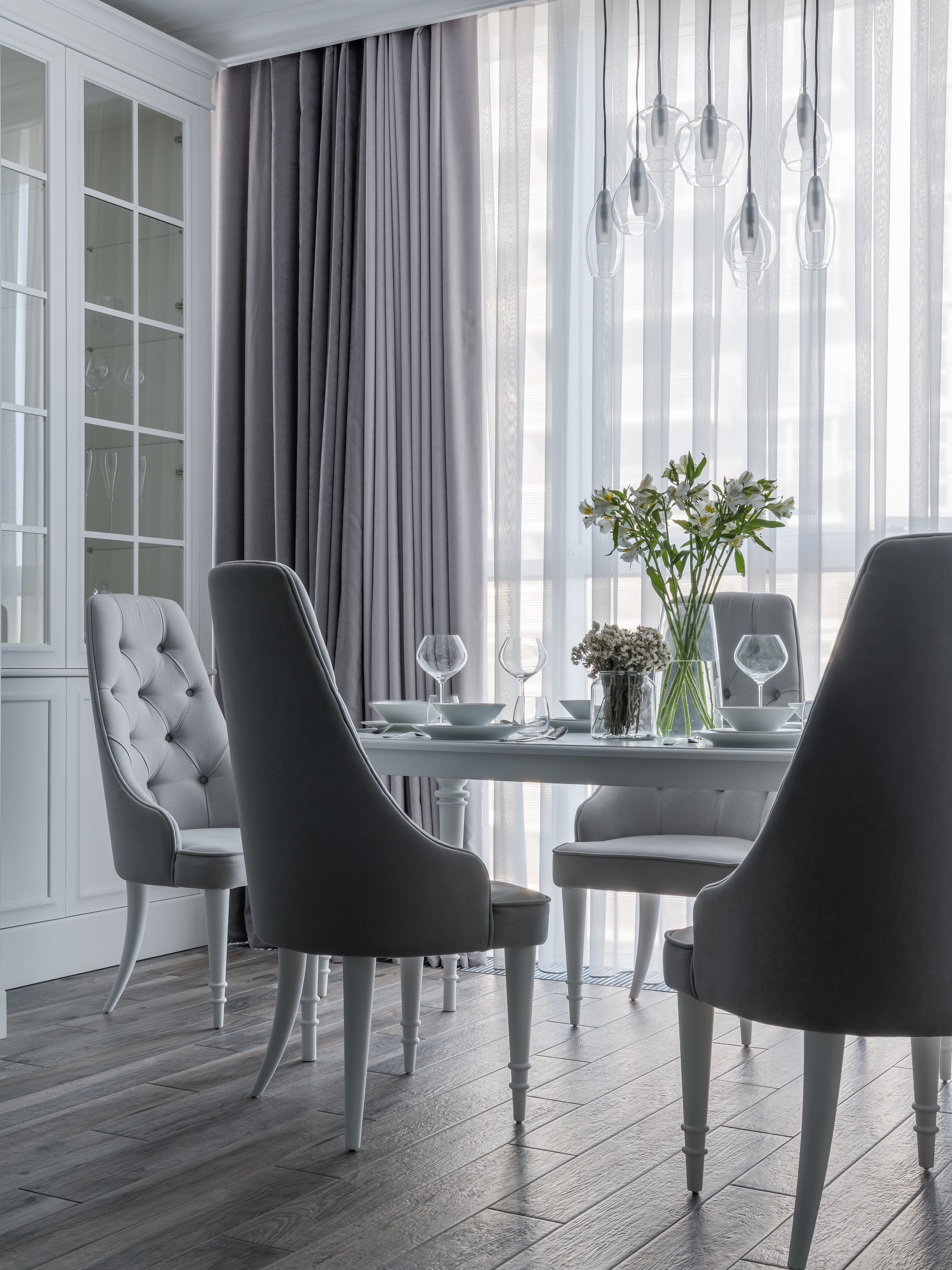 Интерьер светлой столовой с мягкими серыми креслами, белым столом, декоративными светильниками и живыми цветами в вазе, современный дизайн Евгении Княжевой, фото интерьерного фотографа Сергея Денисенко.
