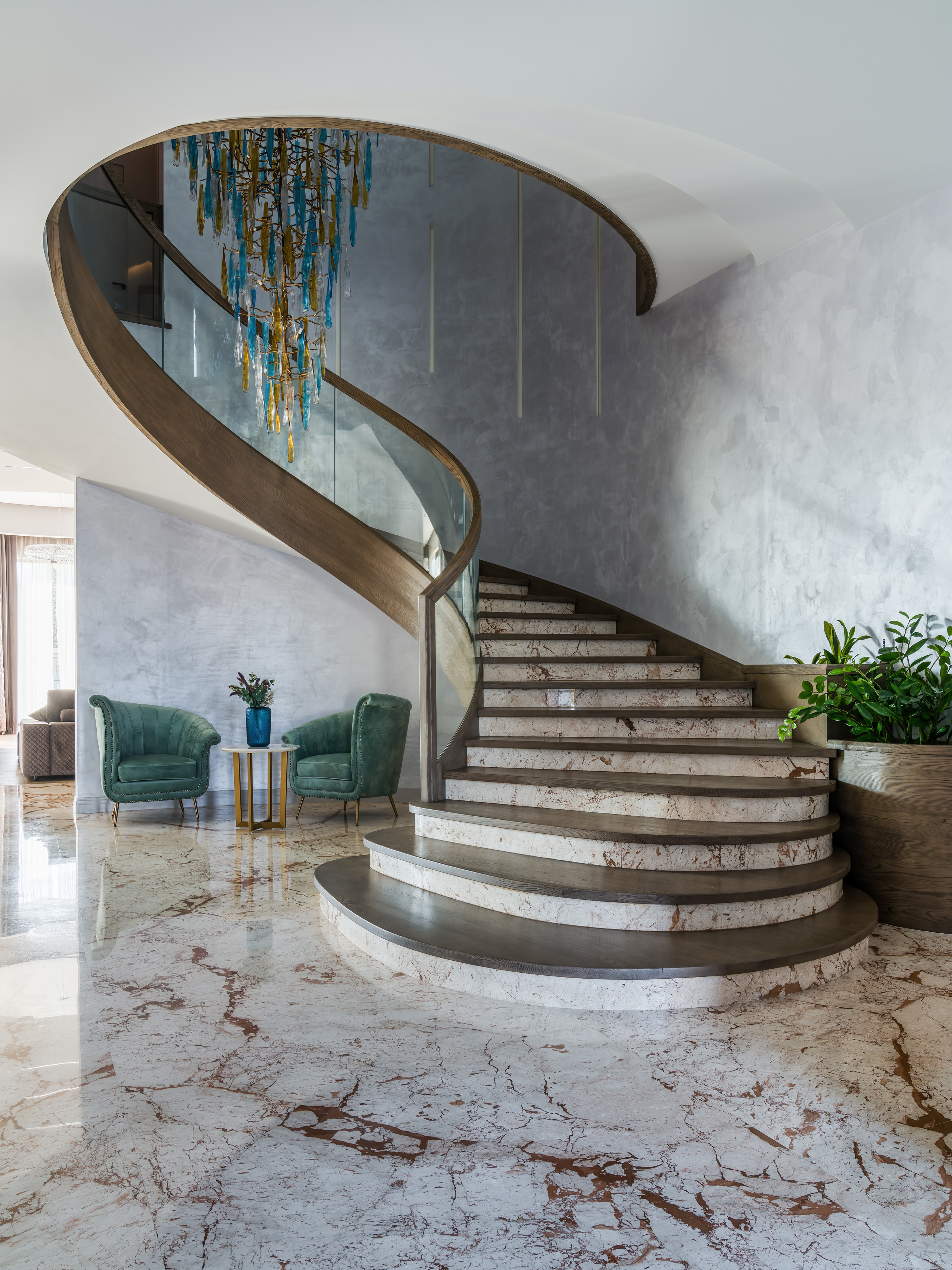 Изящная мраморная лестница с плавным изгибом, стеклянными ограждениями и зоной отдыха, акцент на сочетание светлого камня и современного дизайна, автор проекта Анастасия Ковалевская, интерьерная фотография Сергея Денисенко.