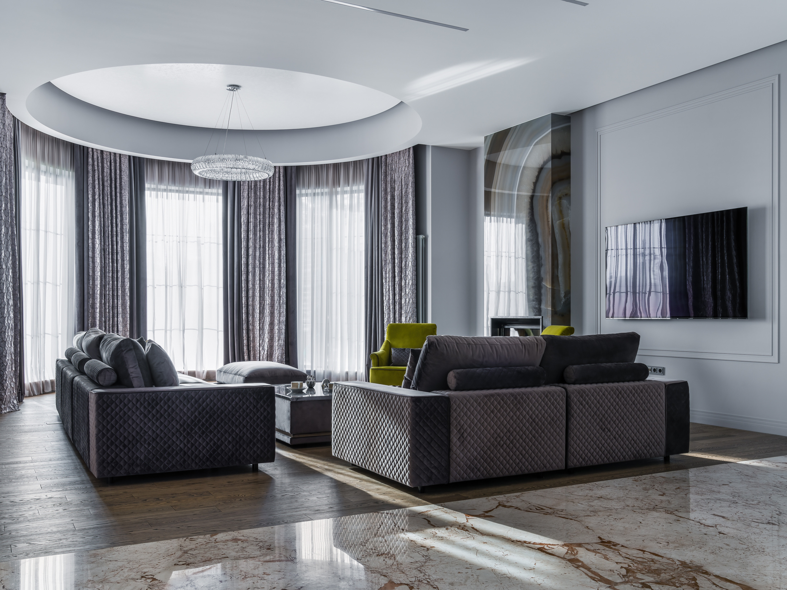 Современная гостиная с панорамными окнами, серыми бархатными диванами и акцентными зелёными креслами, дизайнер Анастасия Ковалевская, фотограф Сергей Денисенко, интерьер с мраморным полом, круговым потолочным светильником и стильным ТВ-зоной.