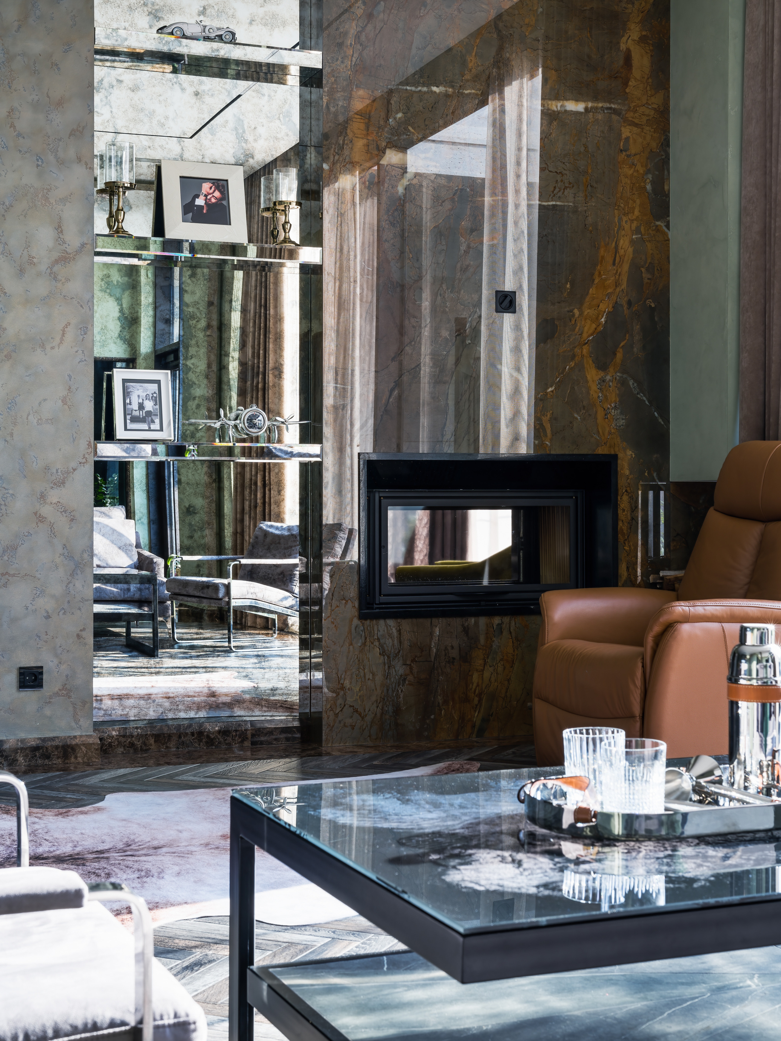Интерьер гостиной с мраморной облицовкой камина, зеркальными полками с фотографиями и аксессуарами, дизайнер Анастасия Ковалевская, фотограф Сергей Денисенко, современный уют с акцентом на каменные текстуры и теплое освещение.