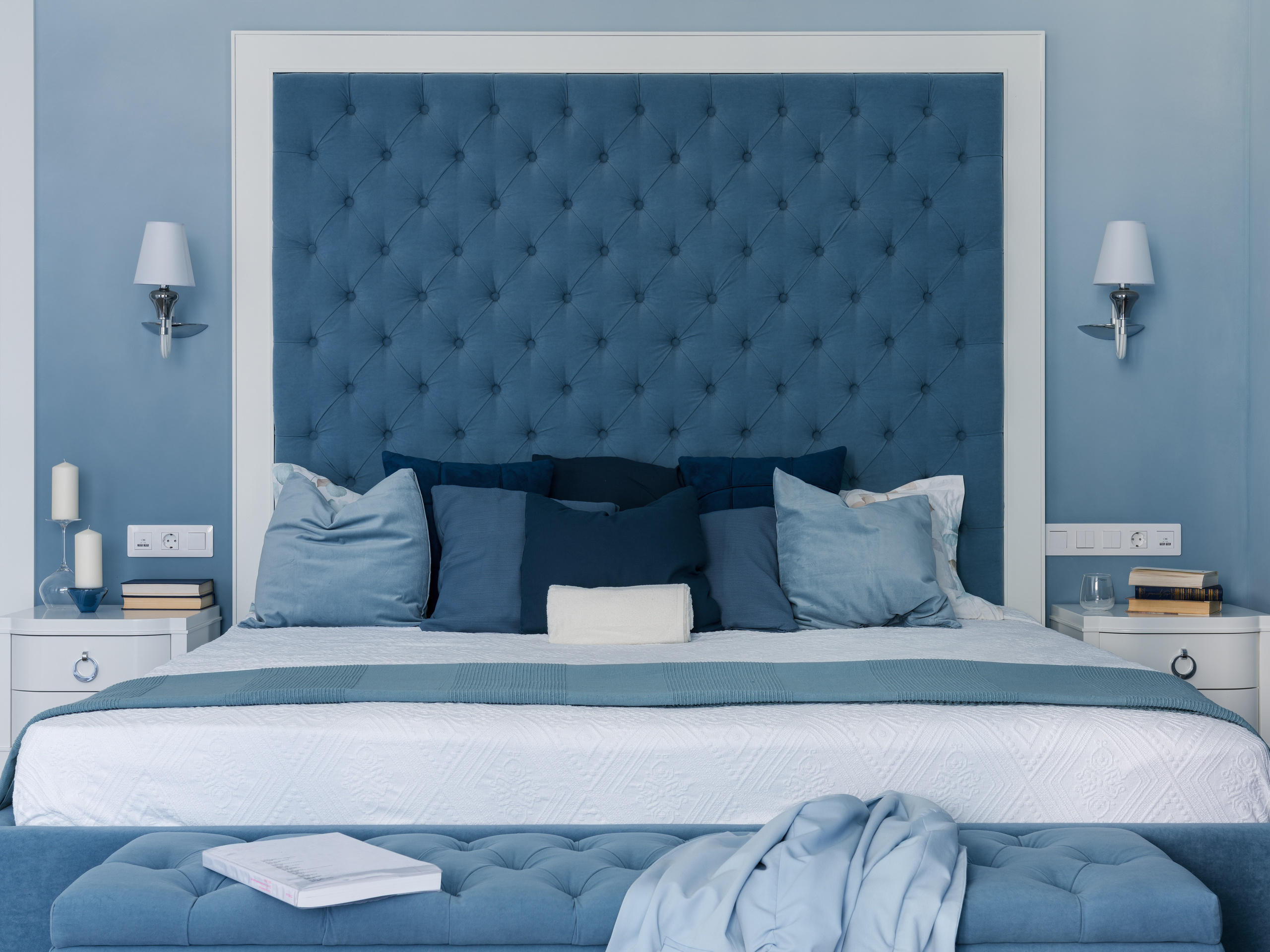 Просторная спальня с кроватью и высоким мягким изголовьем в синей обивке, множеством подушек и симметричными прикроватными тумбами. Автор проекта Евгения Княжева, фотосъёмка Сергей Денисенко.