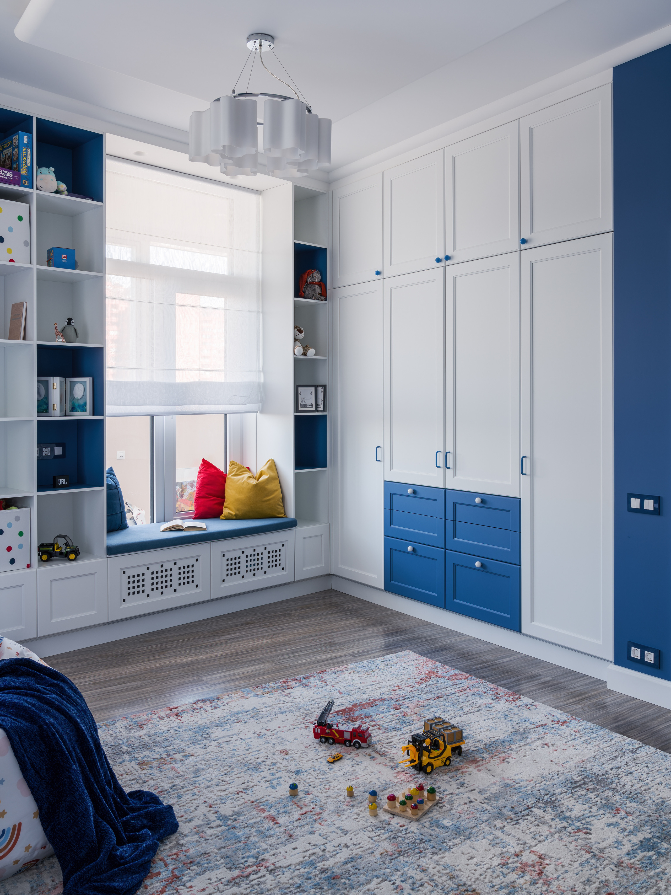 Современная детская с бело-синим шкафом, местом для чтения у окна и ярким ковром с игрушками. Автор дизайна Евгения Княжева, фотограф интерьеров Сергей Денисенко.