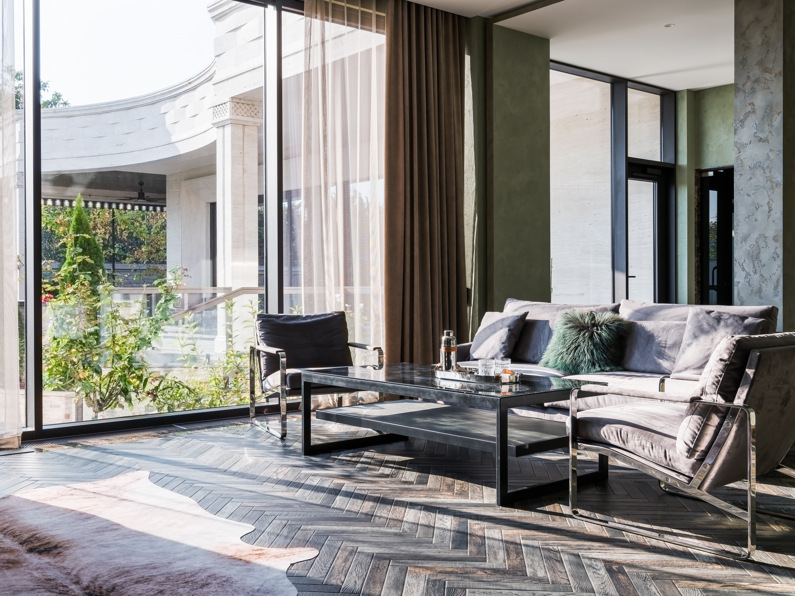 Светлая гостиная с панорамным остеклением, мягким серым диваном, стеклянным журнальным столиком и кожаными креслами, интерьер от дизайнера Анастасии Ковалевской, съемка фотографа Сергея Денисенко, гармония современного стиля и уюта.