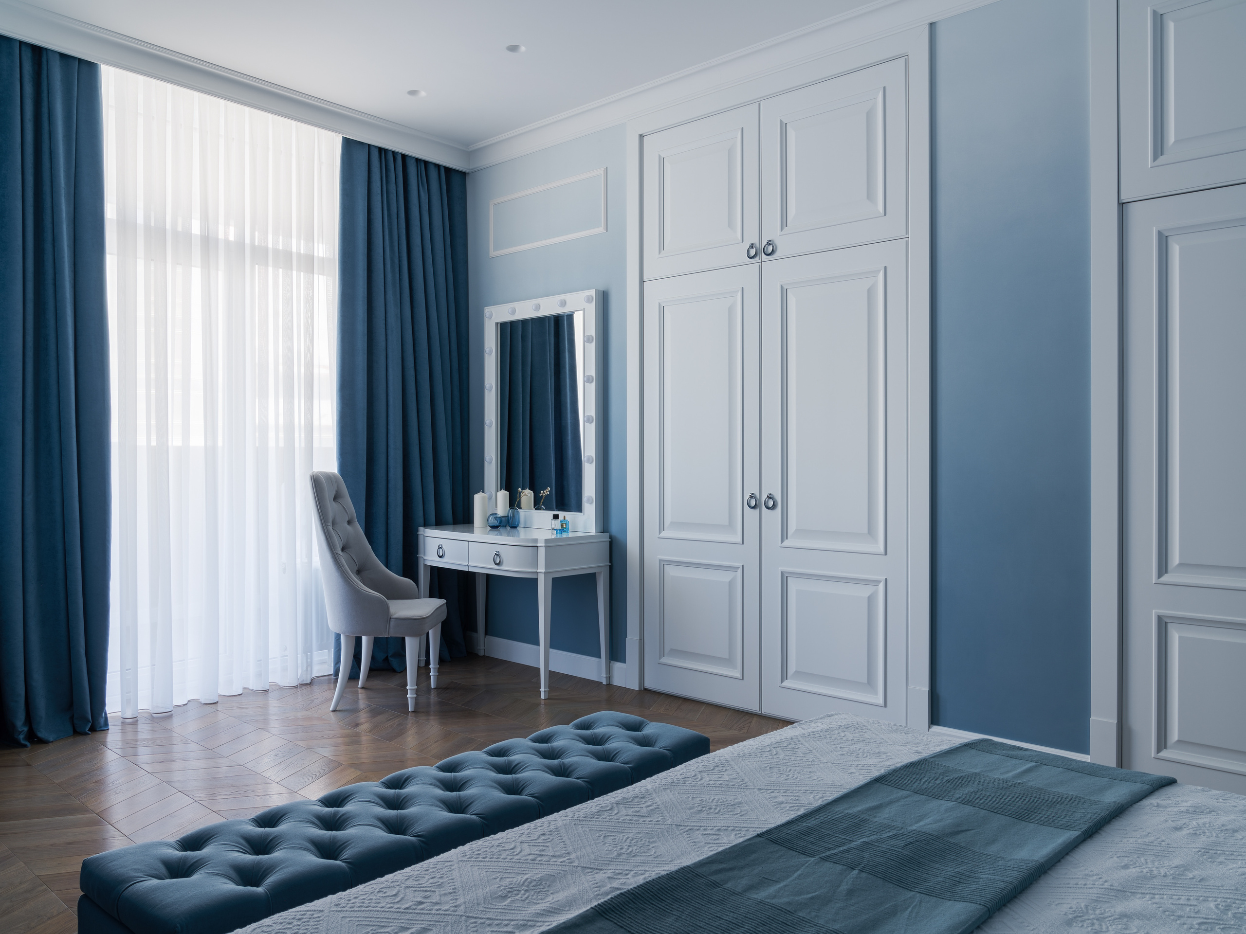 Вид на спальню с белыми шкафами, туалетным столиком с зеркалом и мягким серым креслом, оформленную в спокойных голубых оттенках. Интерьер создан Евгенией Княжевой, фото Сергей Денисенко.