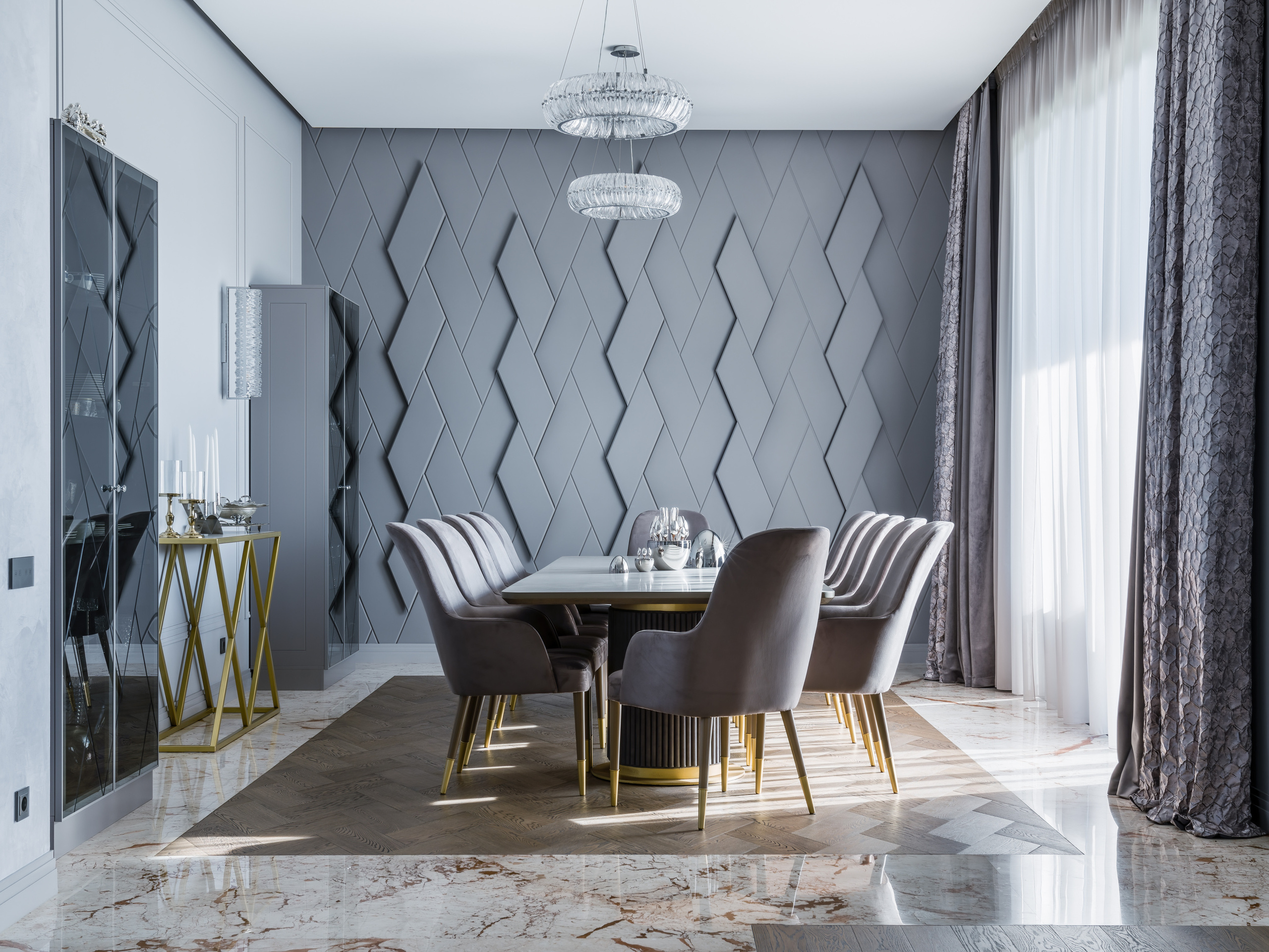 Элегантная столовая с серыми бархатными креслами на золотых ножках, дизайнерским серым 3D-панелированием стены, современными люстрами и мраморным полом; интерьер создан дизайнером Анастасией Ковалевской, фото Сергея Денисенко.