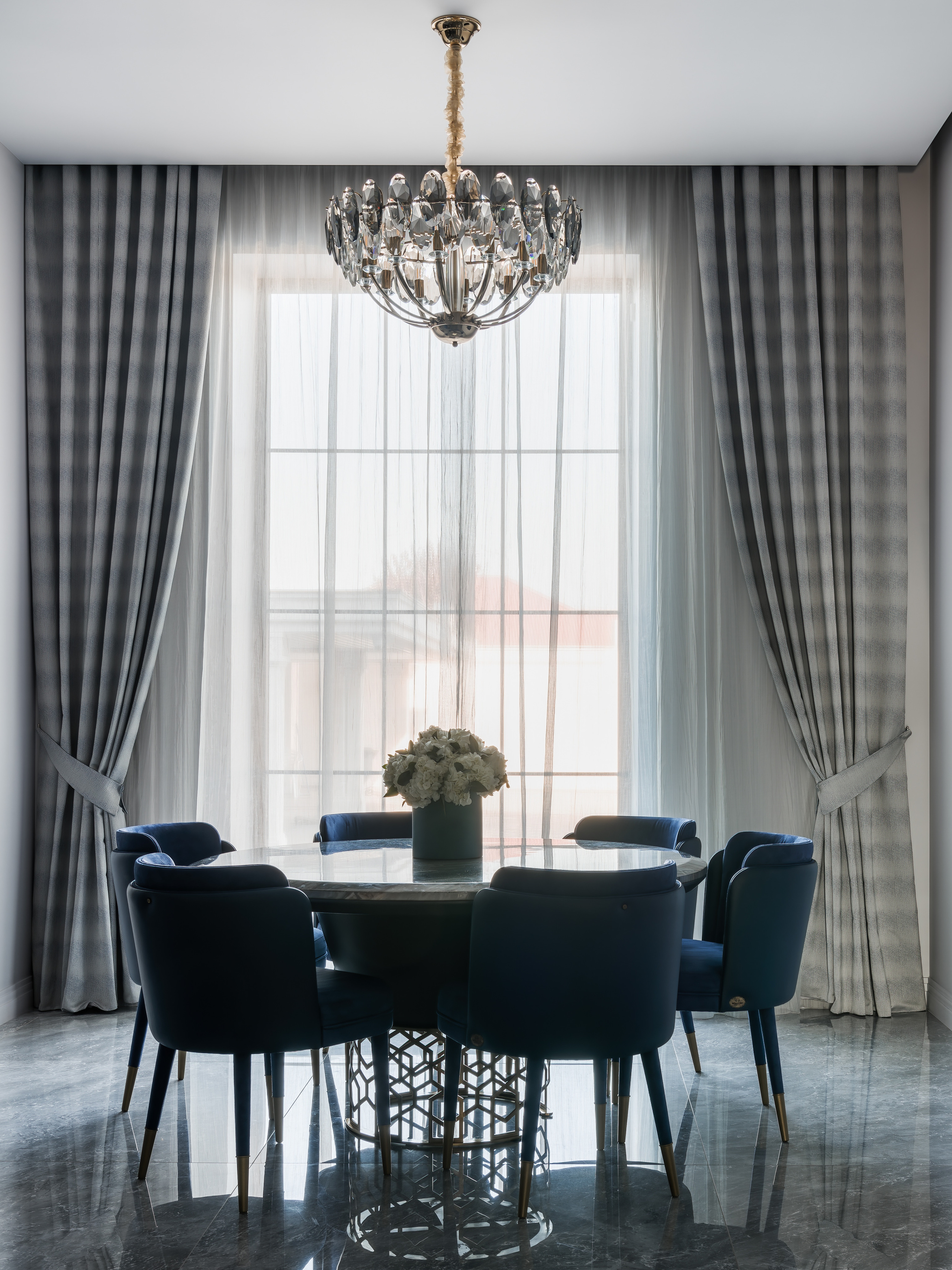 Столовая зона с круглым столом из камня, мягкими креслами глубокого синего цвета и хрустальной люстрой. Интерьер создан дизайнером Анастасией Ковалевской, фото — Сергей Денисенко.