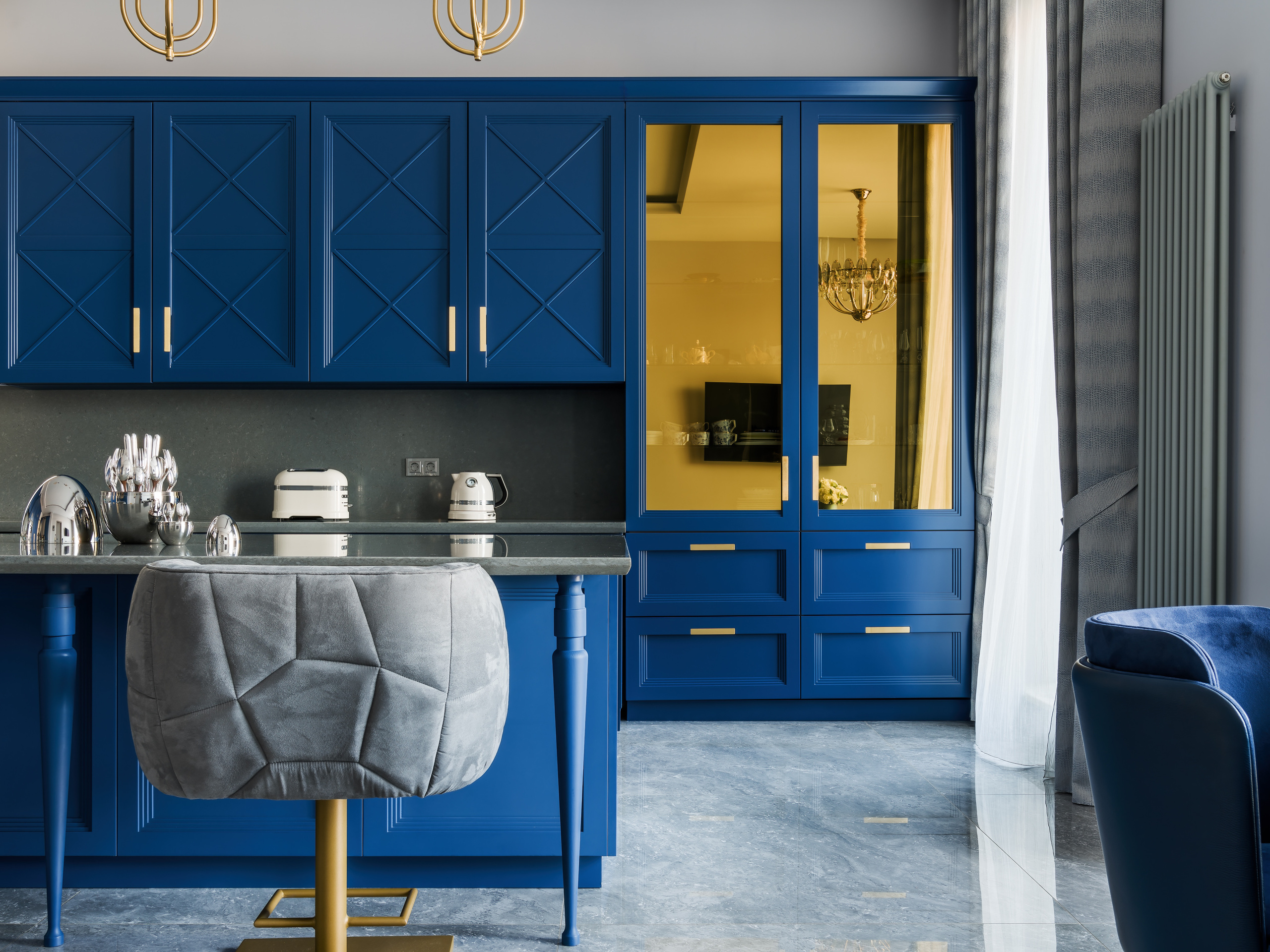 Деталь интерьера кухни с синими фасадами, золотыми ручками и стеклянными вставками, серой барной мебелью и стильными светильниками. Автор проекта — дизайнер Анастасия Ковалевская, фотограф Сергей Денисенко.