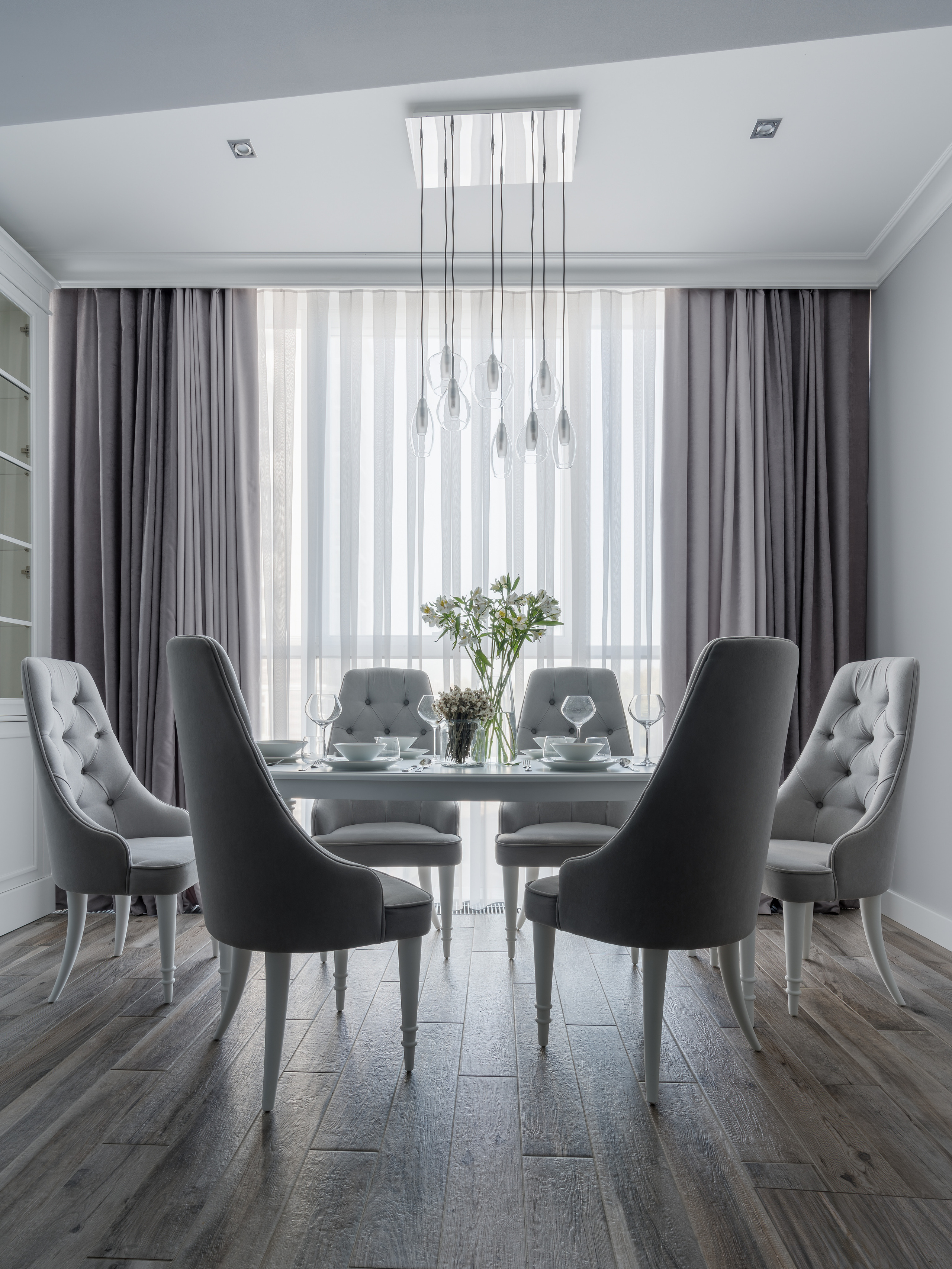 Элегантная столовая с серыми обитыми стульями, круглым столом, светильниками в современном стиле и большими окнами с серыми шторами, дизайн Евгении Княжевой, интерьерная съемка Сергея Денисенко.