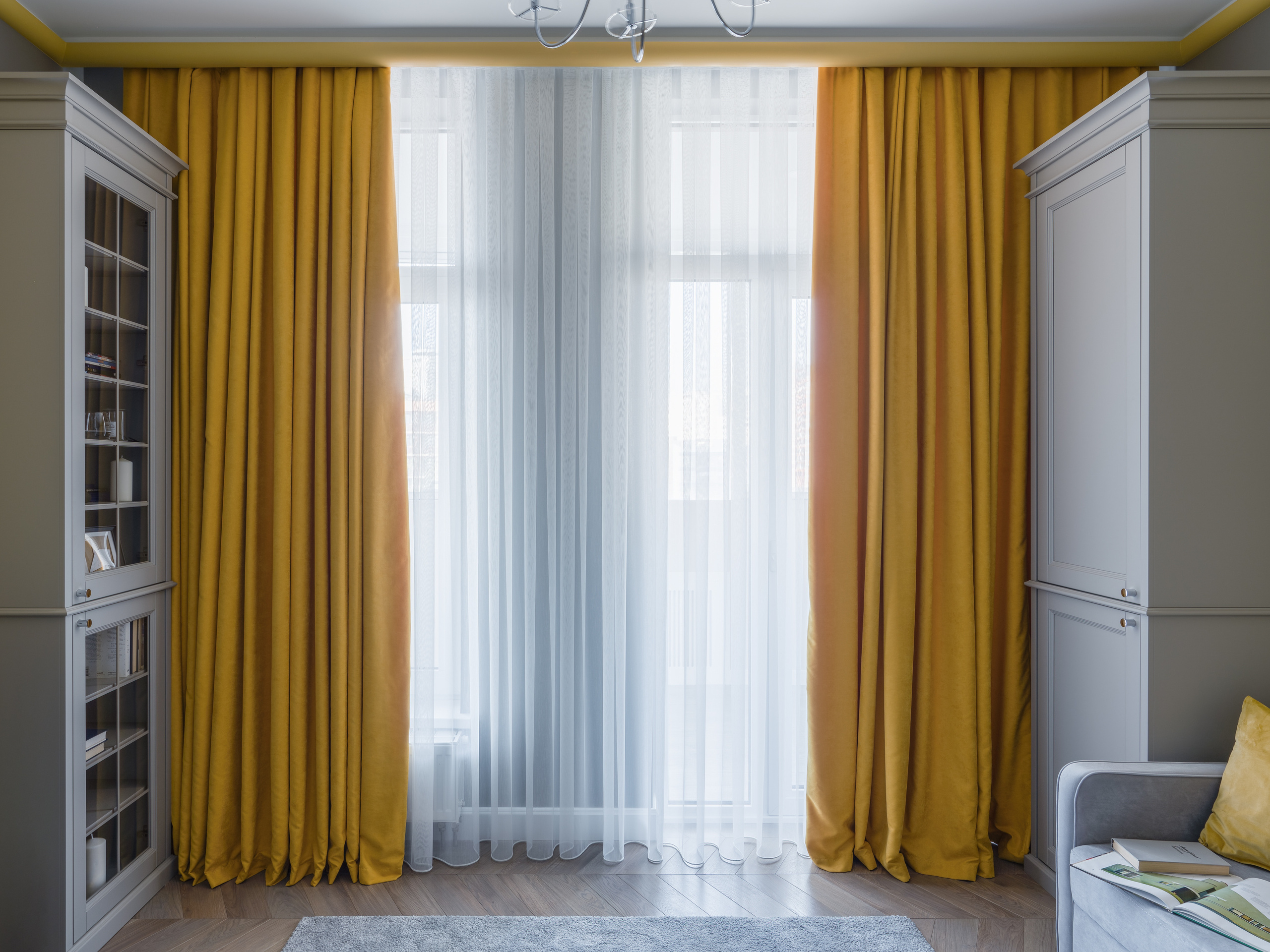 Интерьер гостиной с панорамным окном, плотными жёлтыми шторами и лёгким тюлем, встроенными шкафами и мягким ковром на полу; гармоничный проект Евгении Княжевой, профессиональное фото интерьера Сергей Денисенко.
