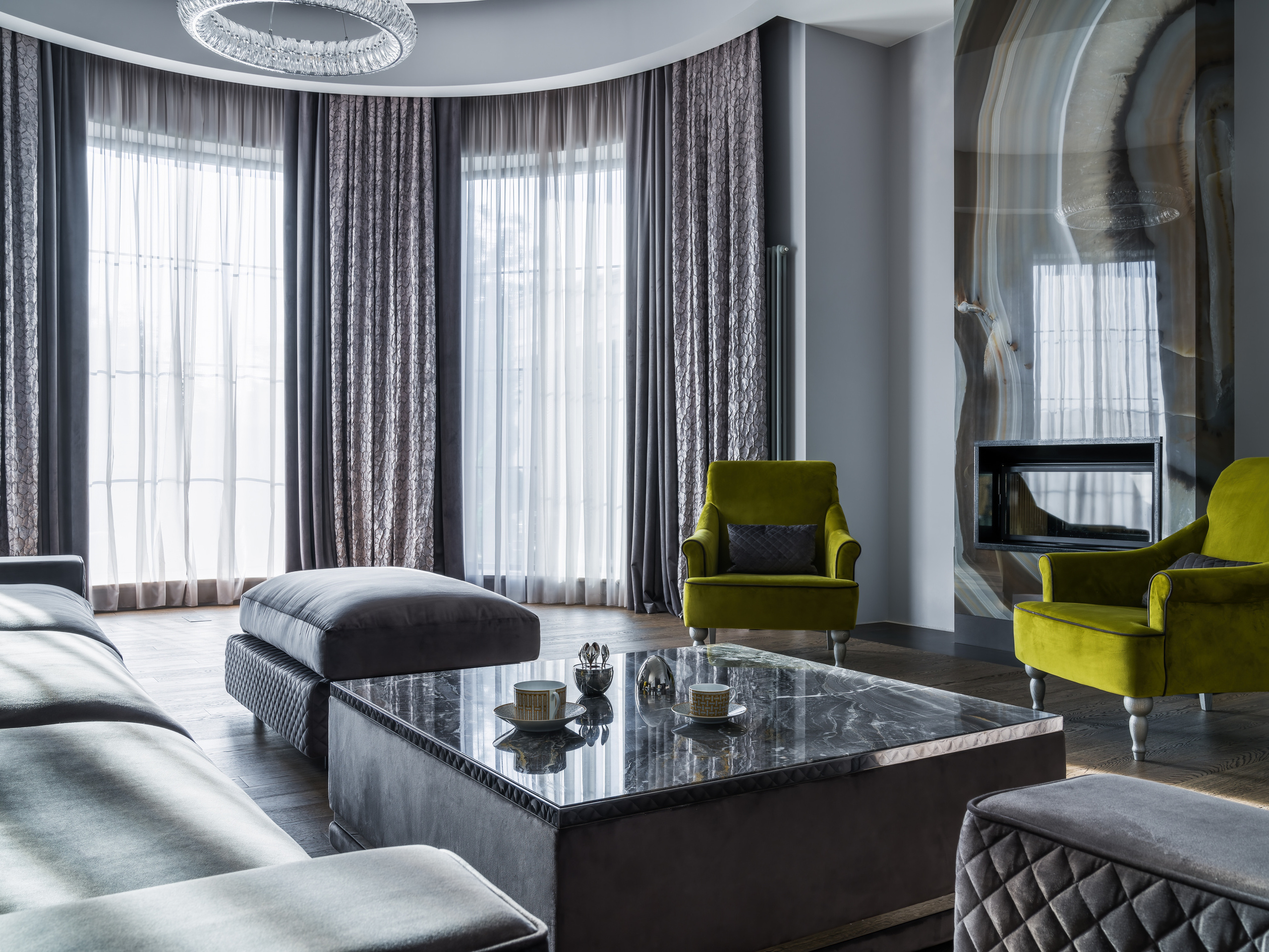 Центральная зона гостиной с мраморным журнальным столиком, серым диваном и зелёными креслами на фоне дизайнерского камина и панорамных окон; интерьер Анастасии Ковалевской, фотосъёмка Сергея Денисенко.