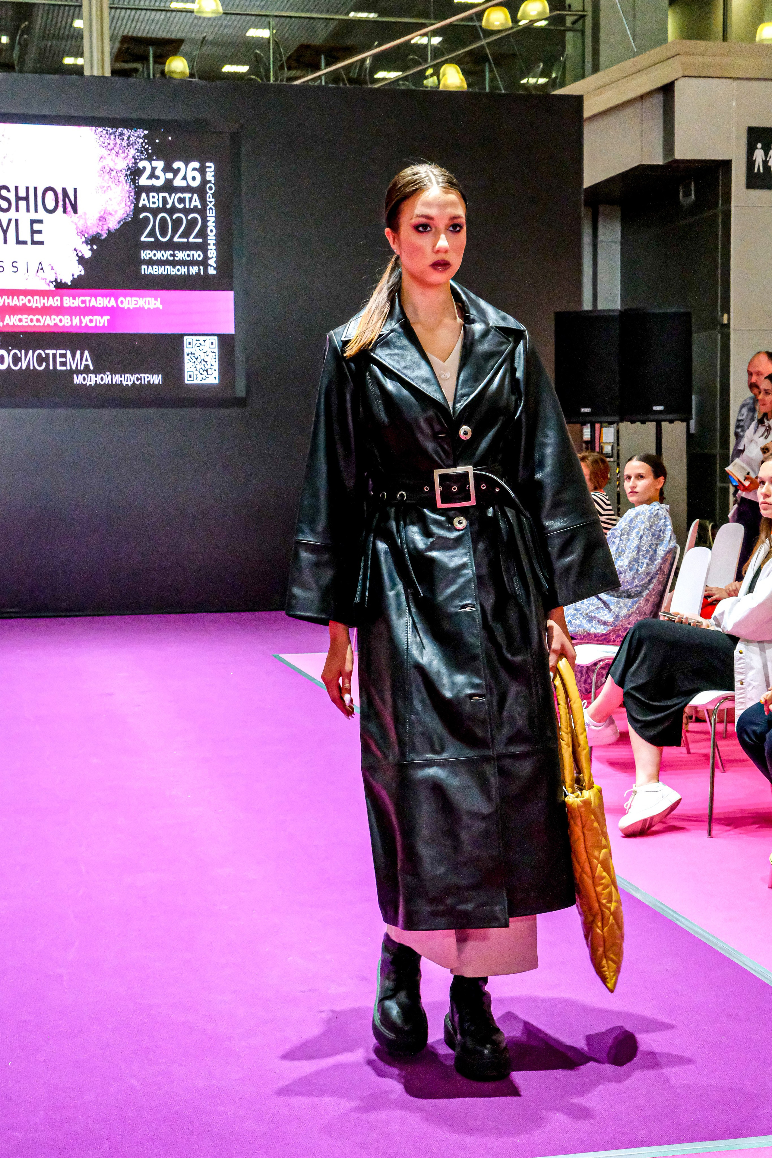  "Модели в ярких нарядах проходят по подиуму во время показа мод, освещенные яркими софитами и окруженные восторженными зрителями."