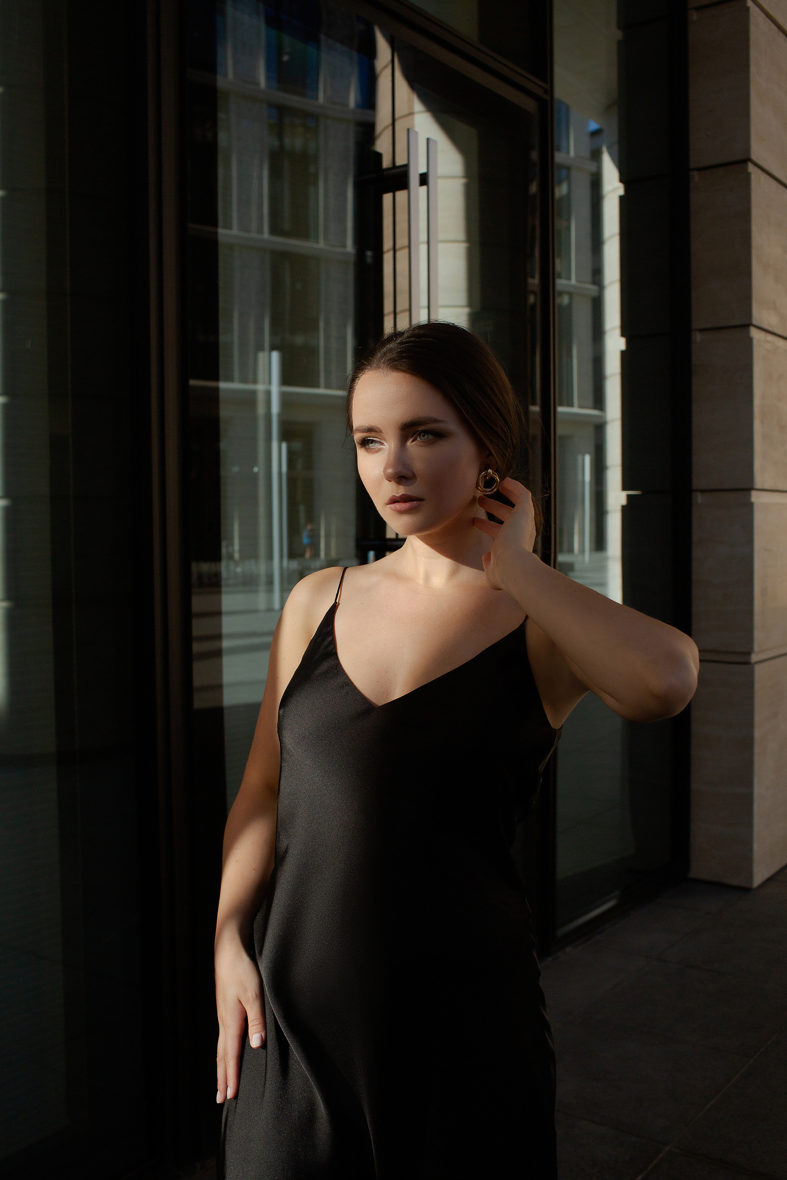 портрет девушки в черном атласном платье в тени на фоне здания