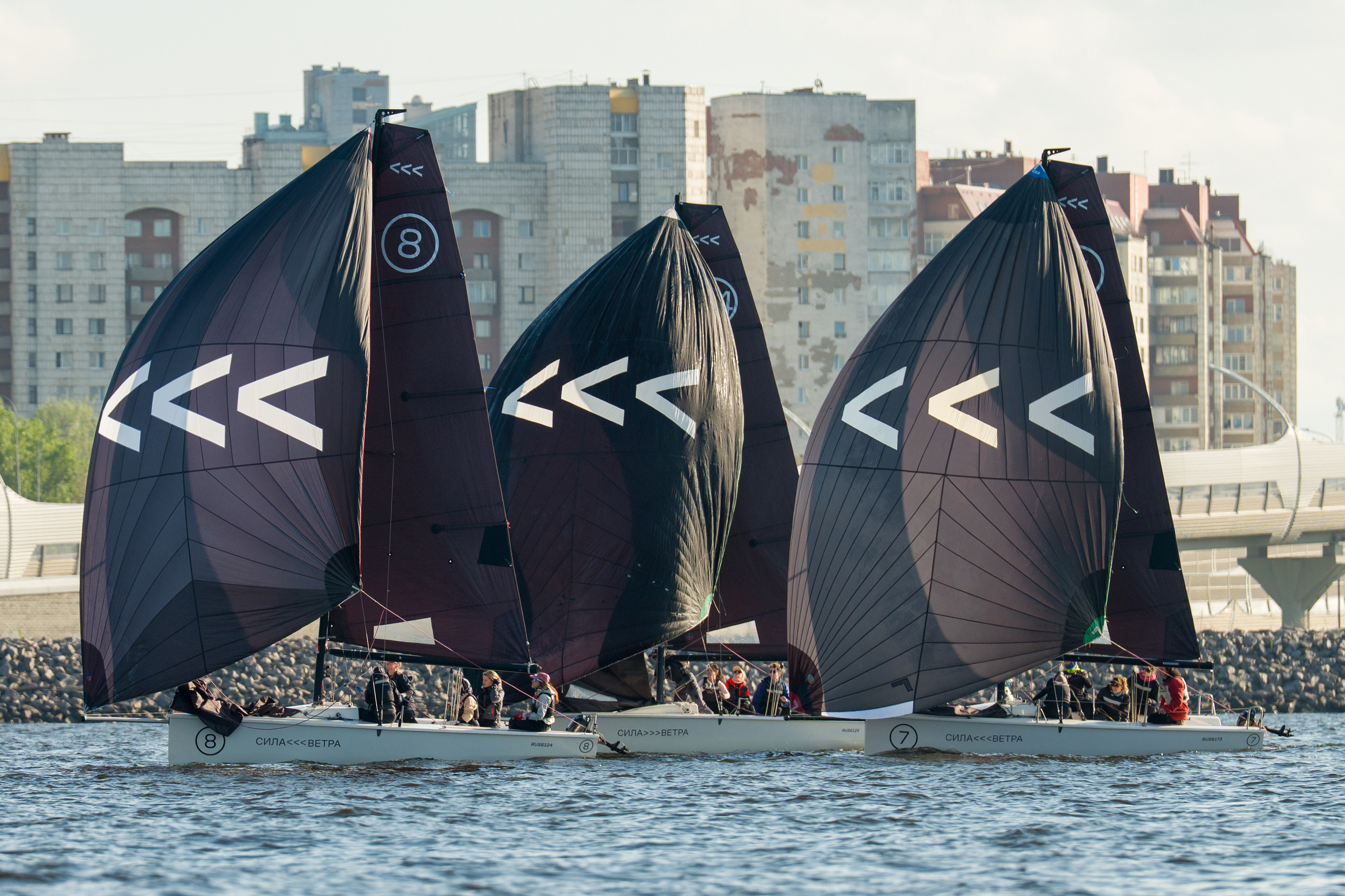 Three SV20s run under black spinnakers along the city waterfront