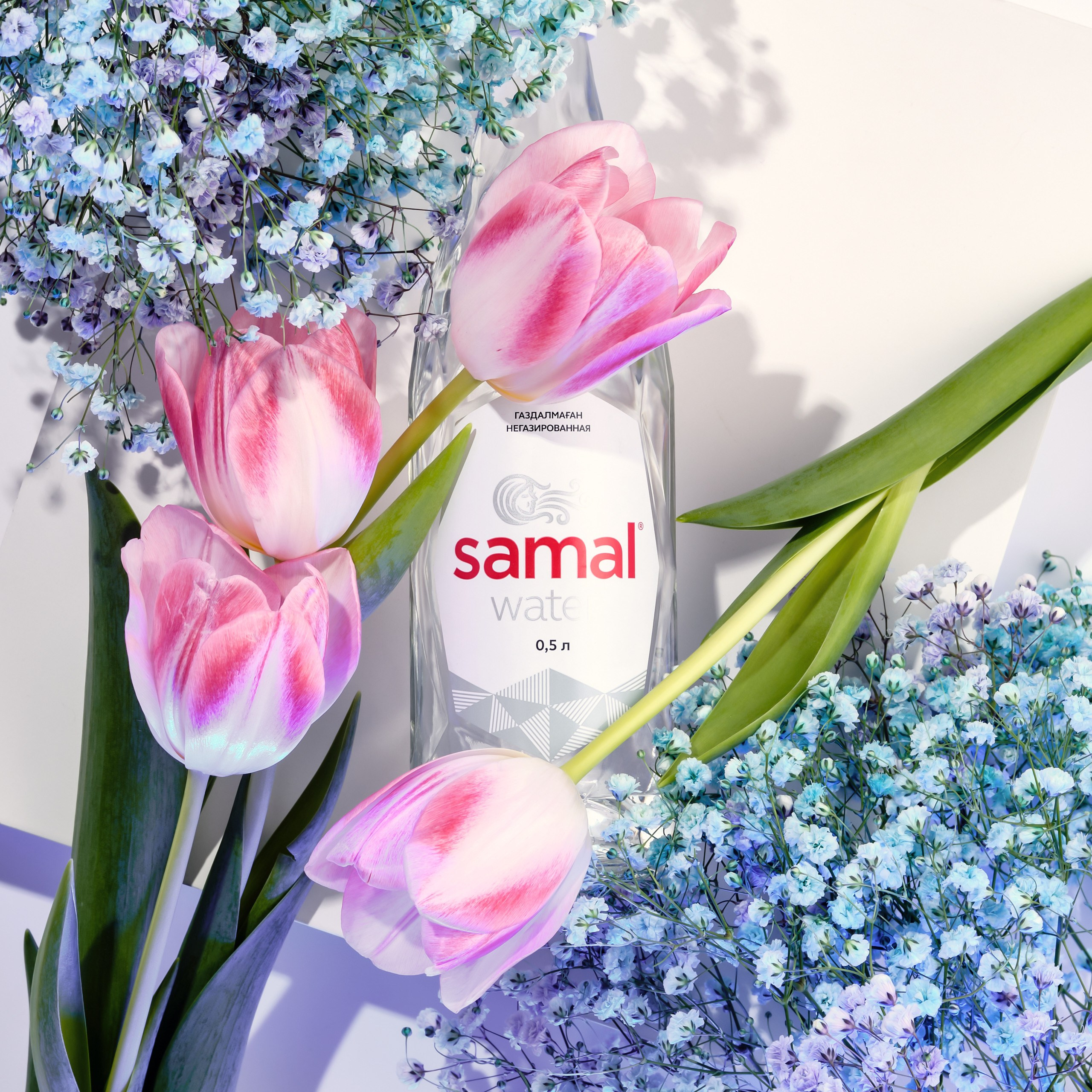 Бутылка воды Samal среди цветов — съёмка с мягким светом и атмосферной подачей
