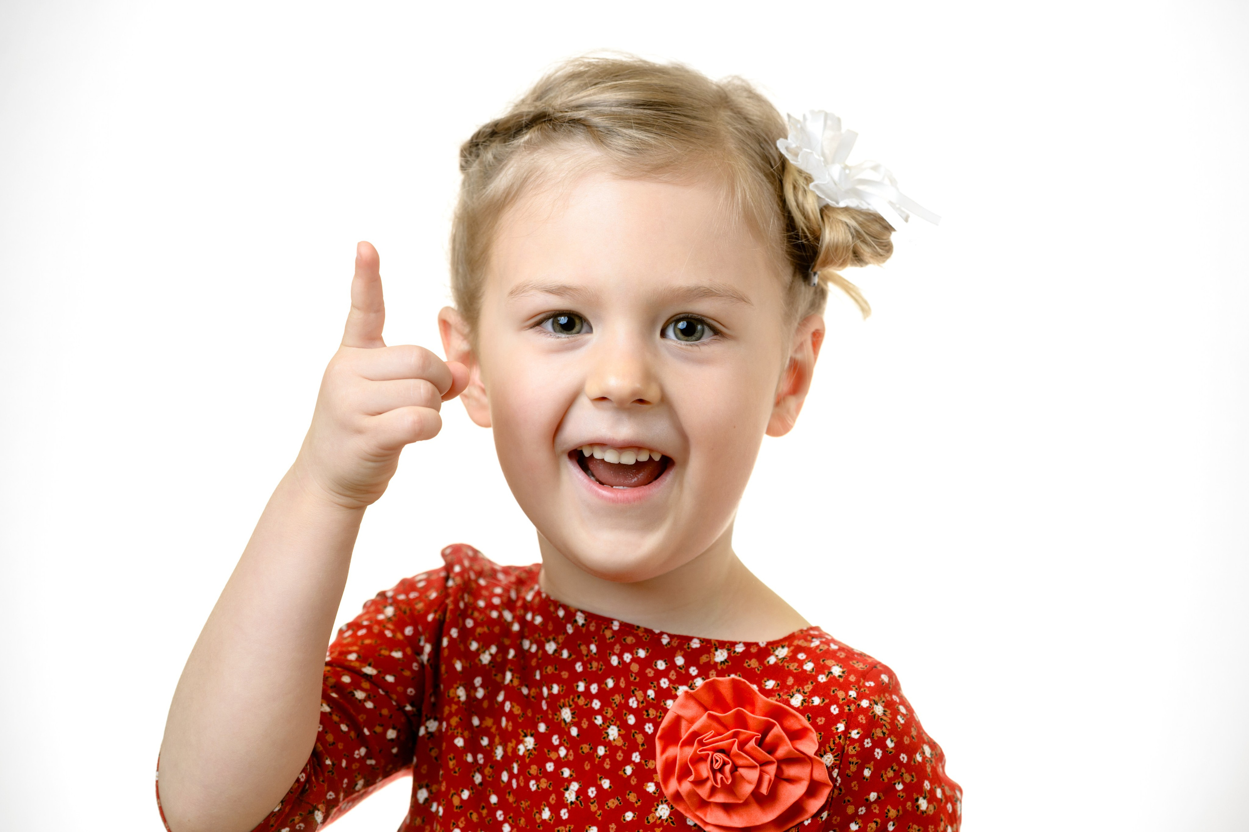 Девочка в красном платье в горошек поднимает палец вверх и улыбается в студийном кадре на белом фоне.