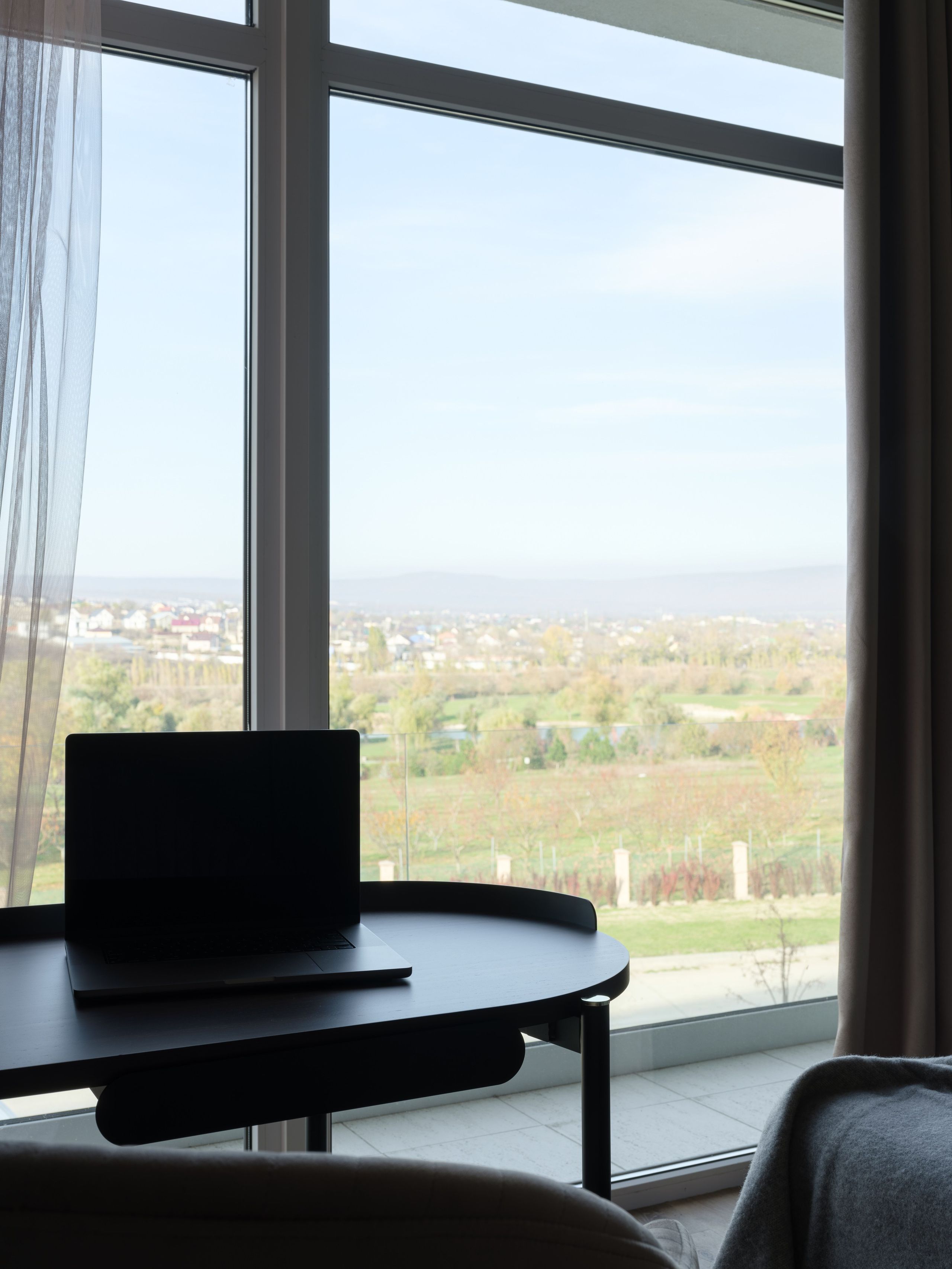 Рабочая зона у панорамного окна с видом на зелёные холмы, чёрным письменным столом и ноутбуком. Элегантный интерьер спальни от дизайнера Алины Дёровой, стилист Наталья Якушева, фотограф Сергей Денисенко.