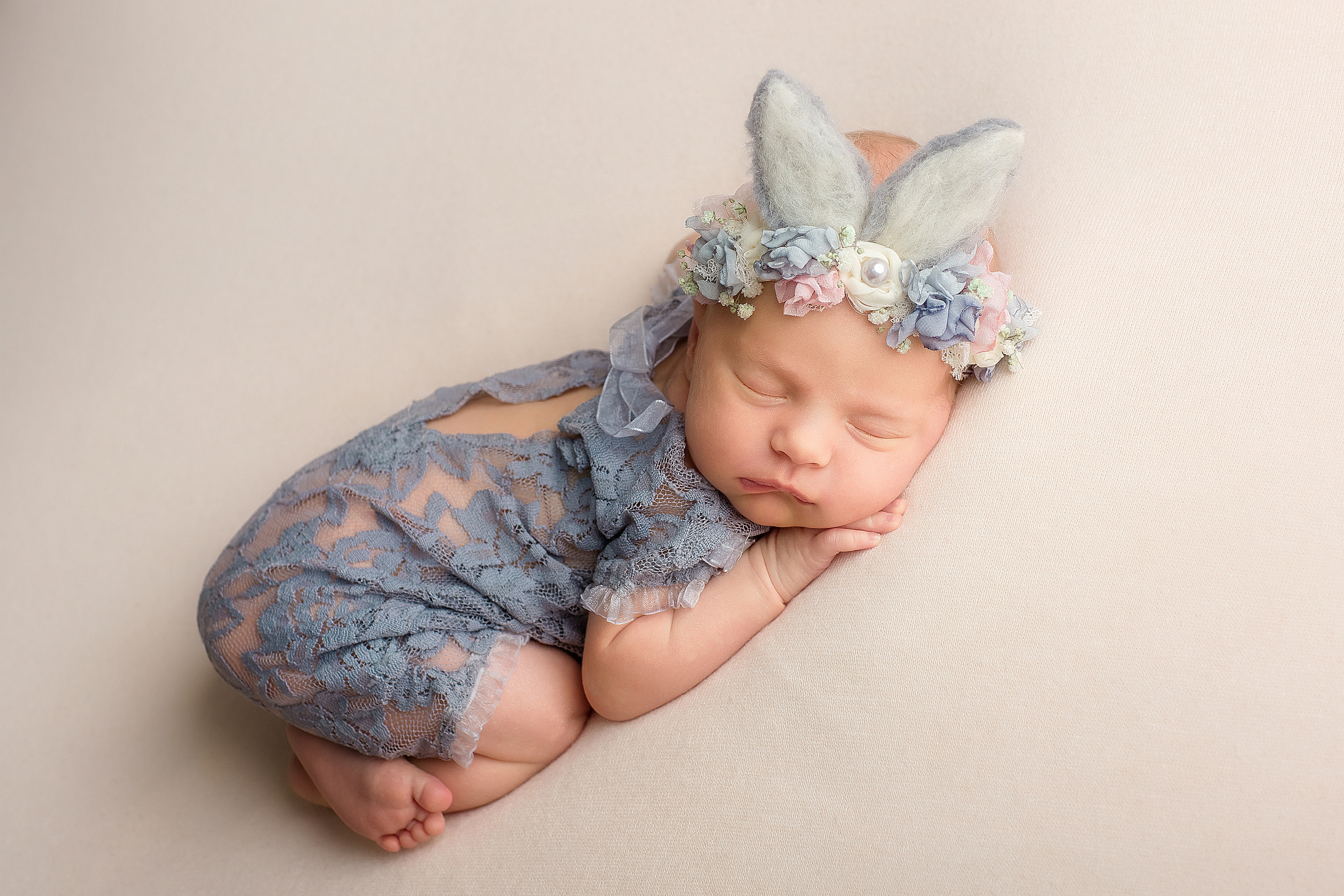 новорожденная малышка в гипюровом голубом бодике в ободочке с ушками зайчика на белом фоне 