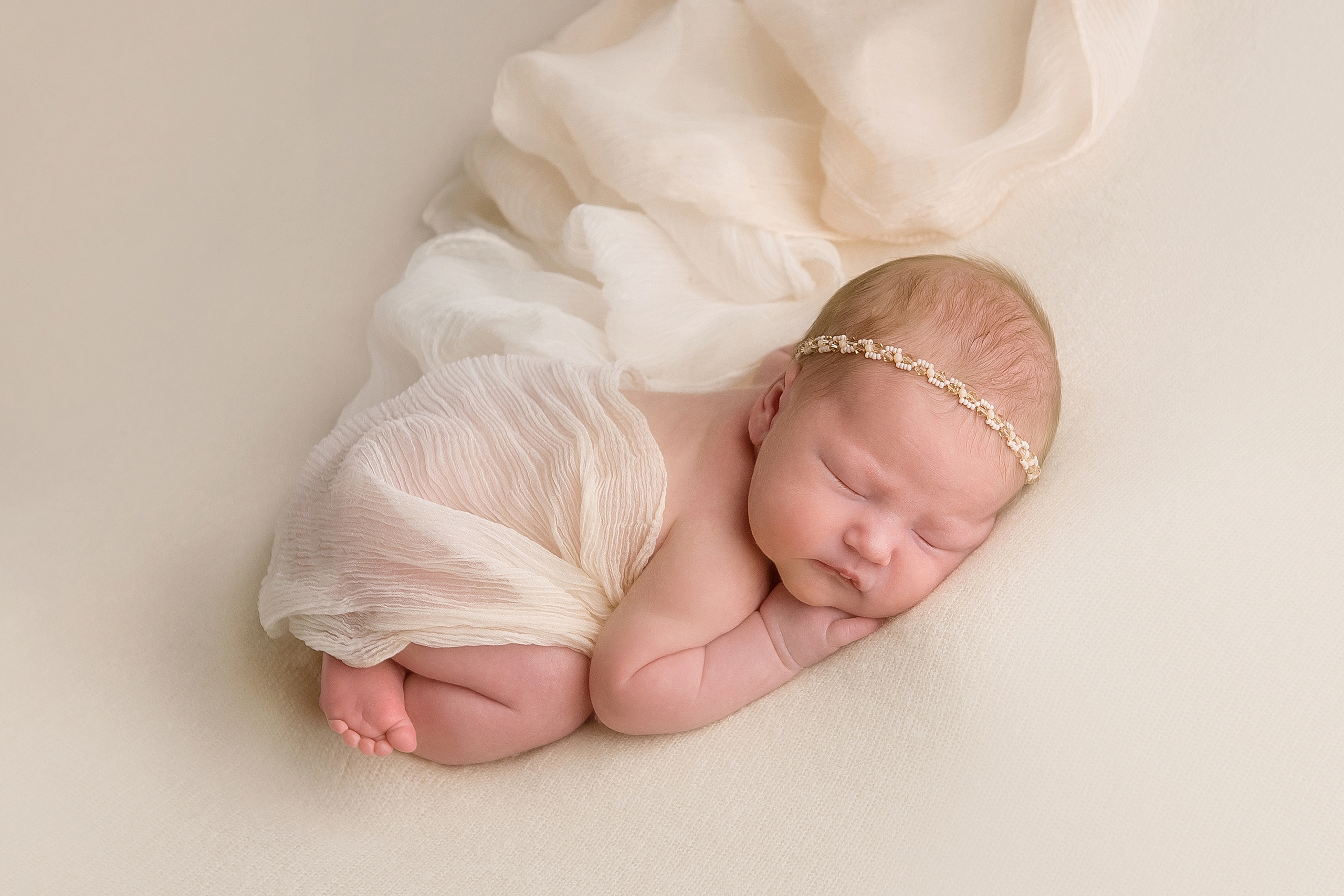 новорожденная малышка позировка на животике на подушке ручки под подбородком на белом фоне