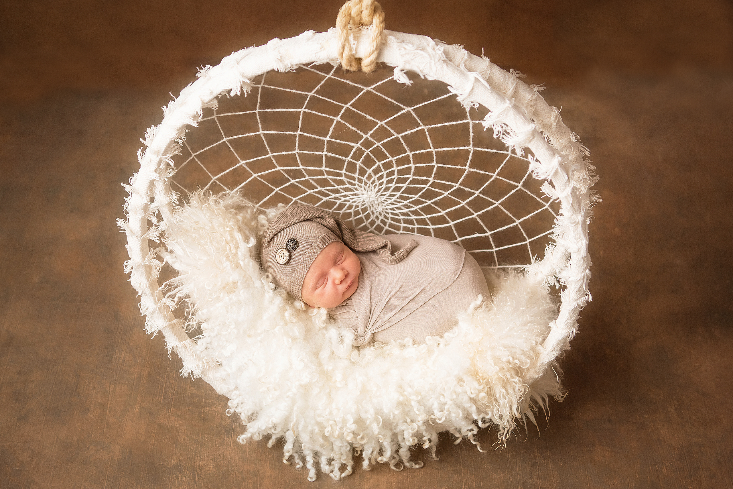 новорожденный малыш в корзинке с магическим талисманом индейцев ловцом снов на коричневом фоне 