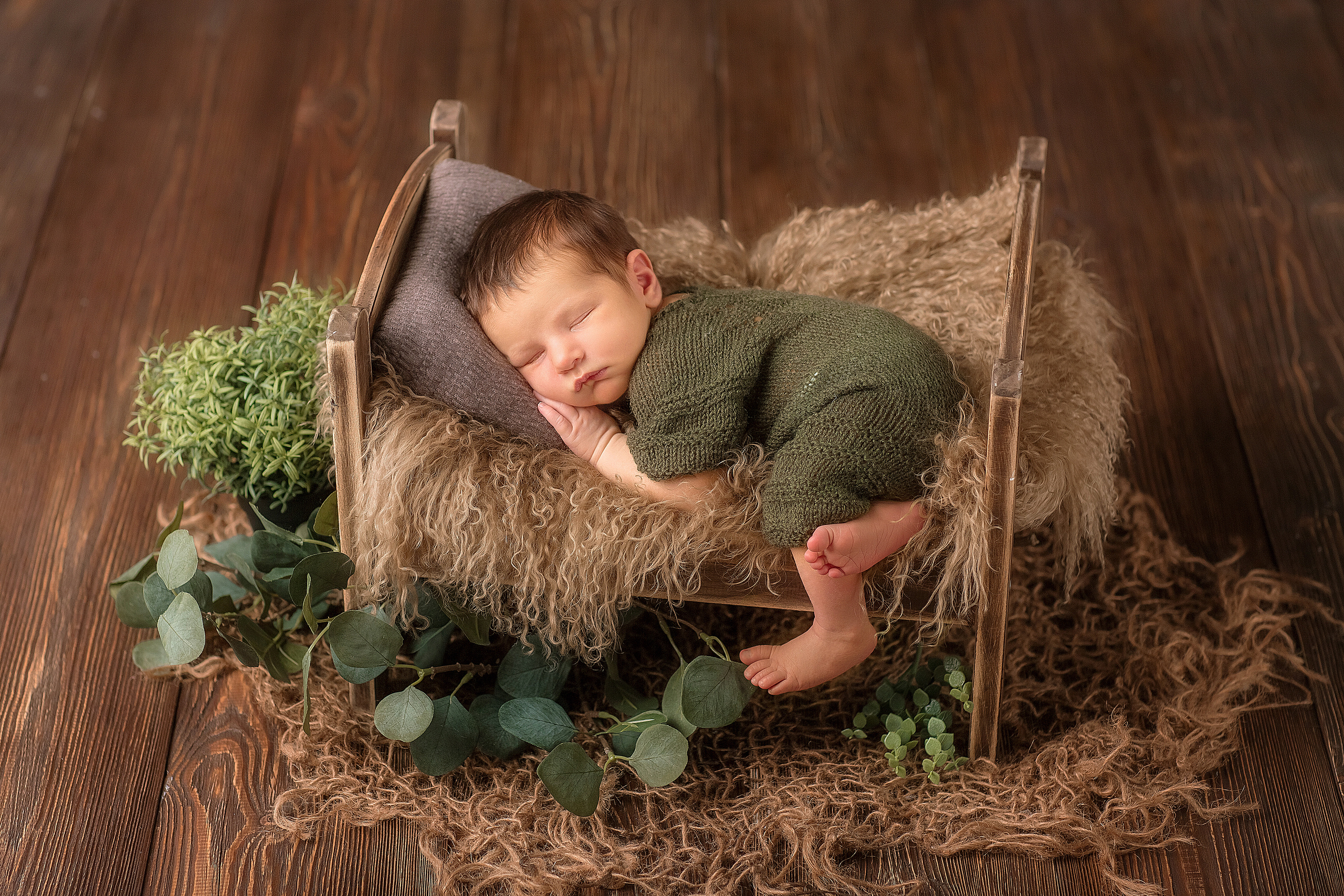 новорожденный малыш в удобной и естественной позе на маленькой кроватке, одна ножка свисает