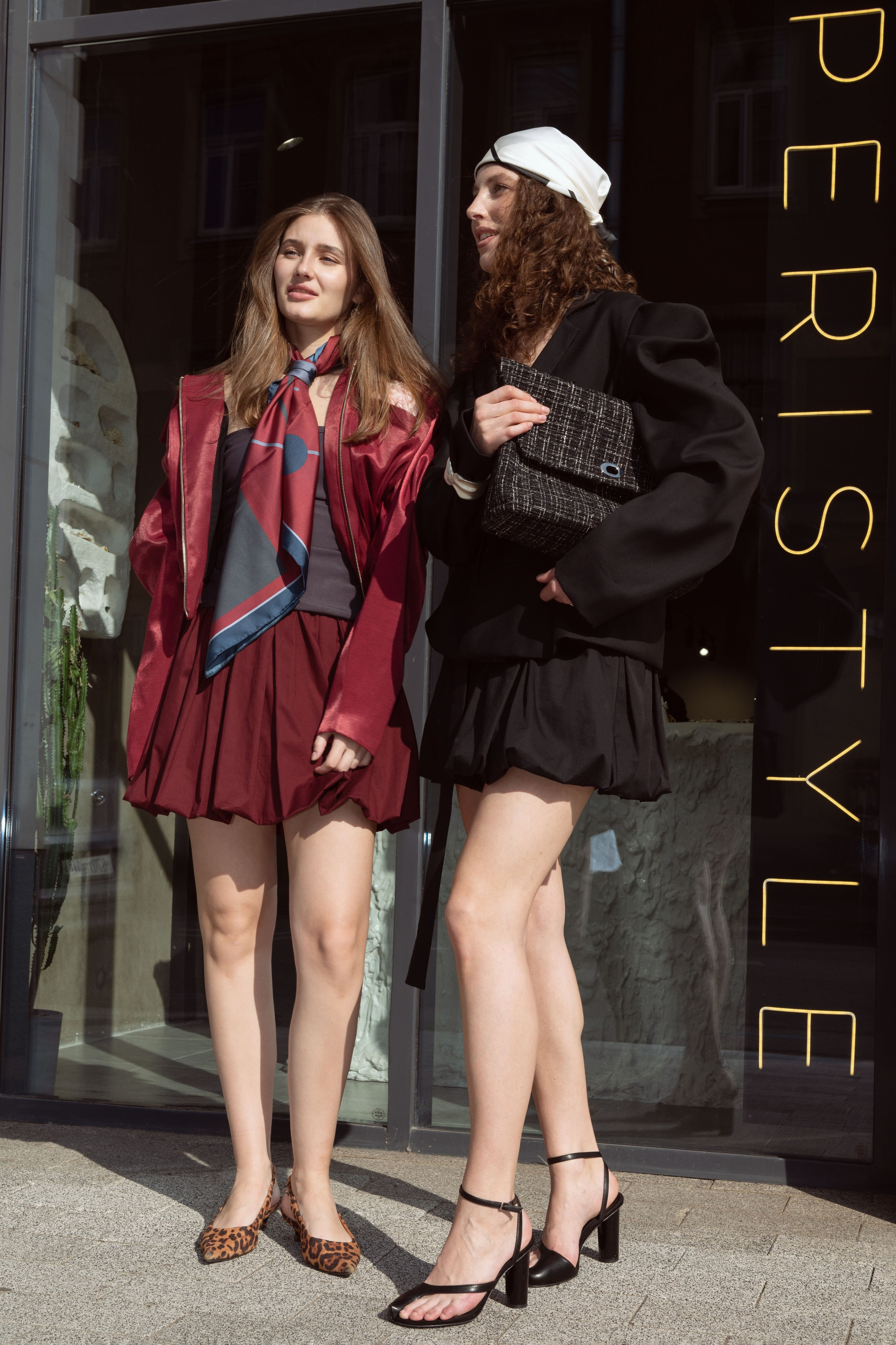 Две красивые девушки в дизайнерской одежде и шелковых дизайнерских платках стоят на фоне витрины бутика
