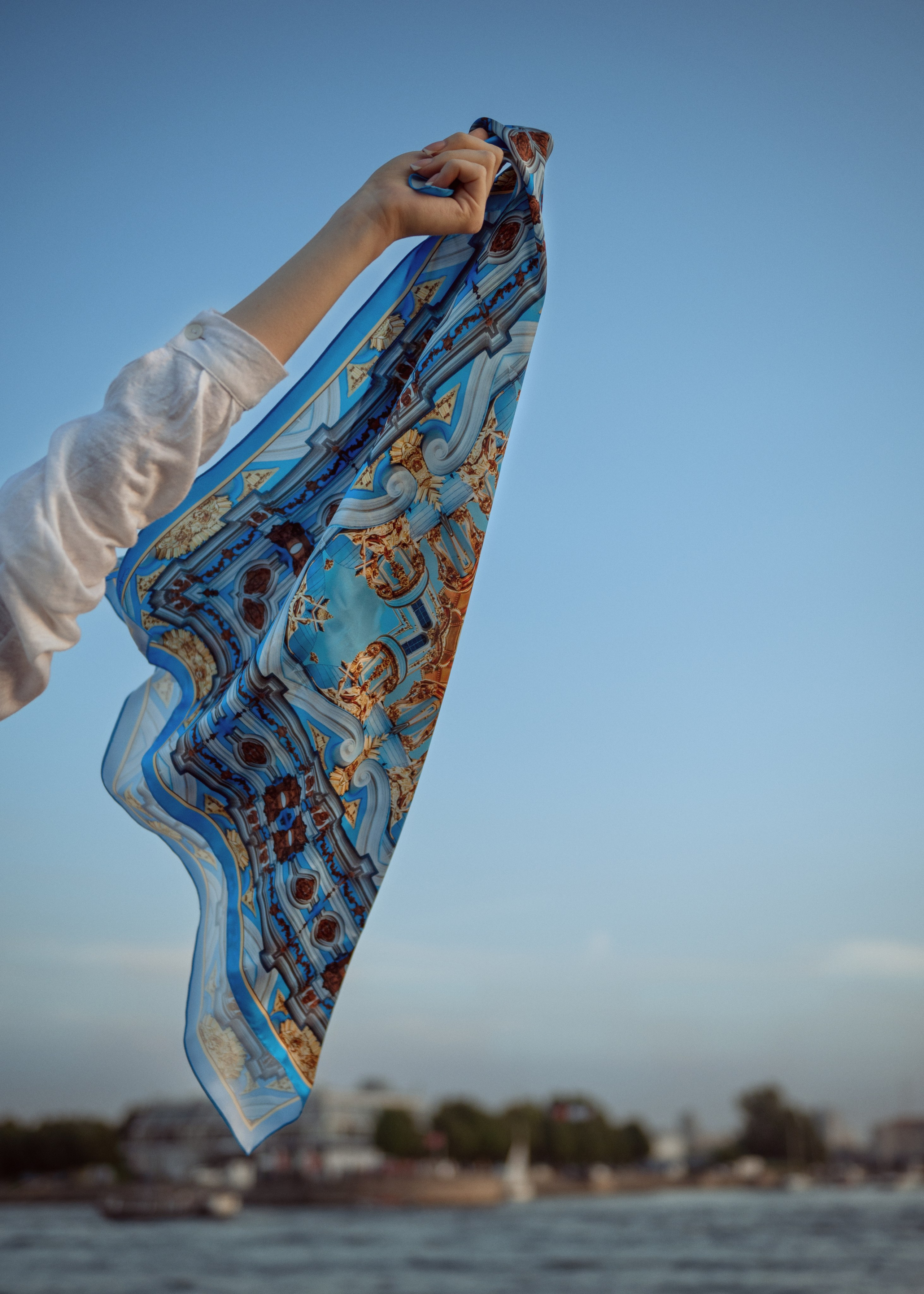 Голубой платок с золотым узором развевается в руке девушки на фоне голубого неба