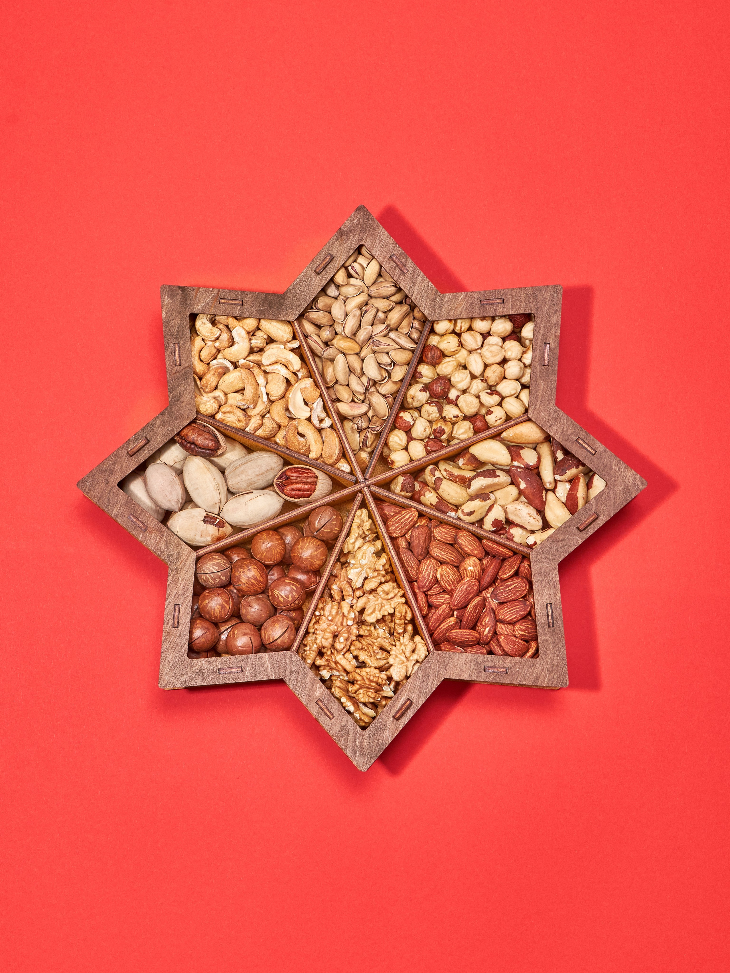 Предметная каталожная фотосъёмка большого подарочного набора орехов и сухофруктов в деревянной коробке в форме звезды на красном фоне