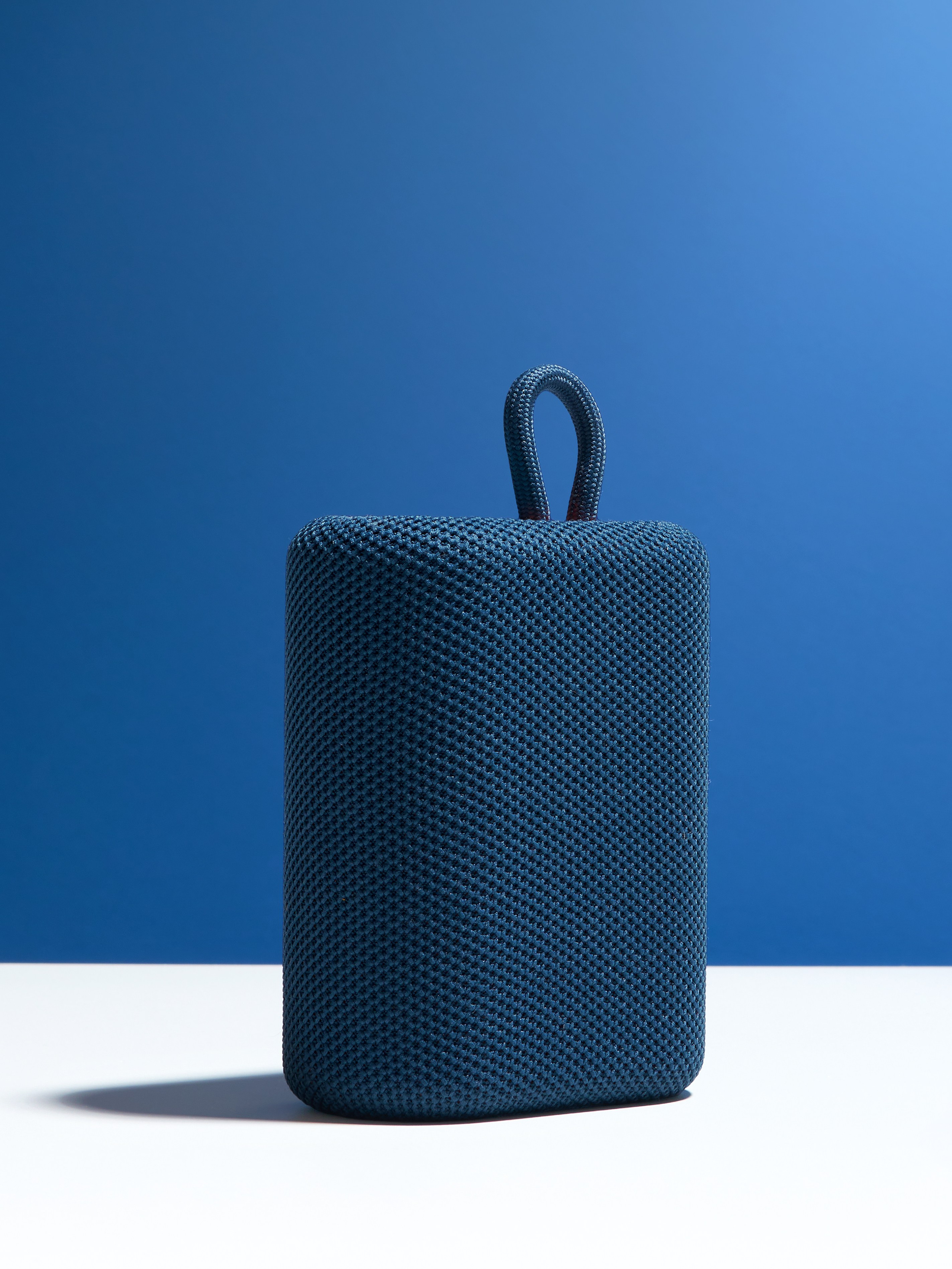 Предметная рекламная фотосъёмка синей колонки на белом и синем фоне