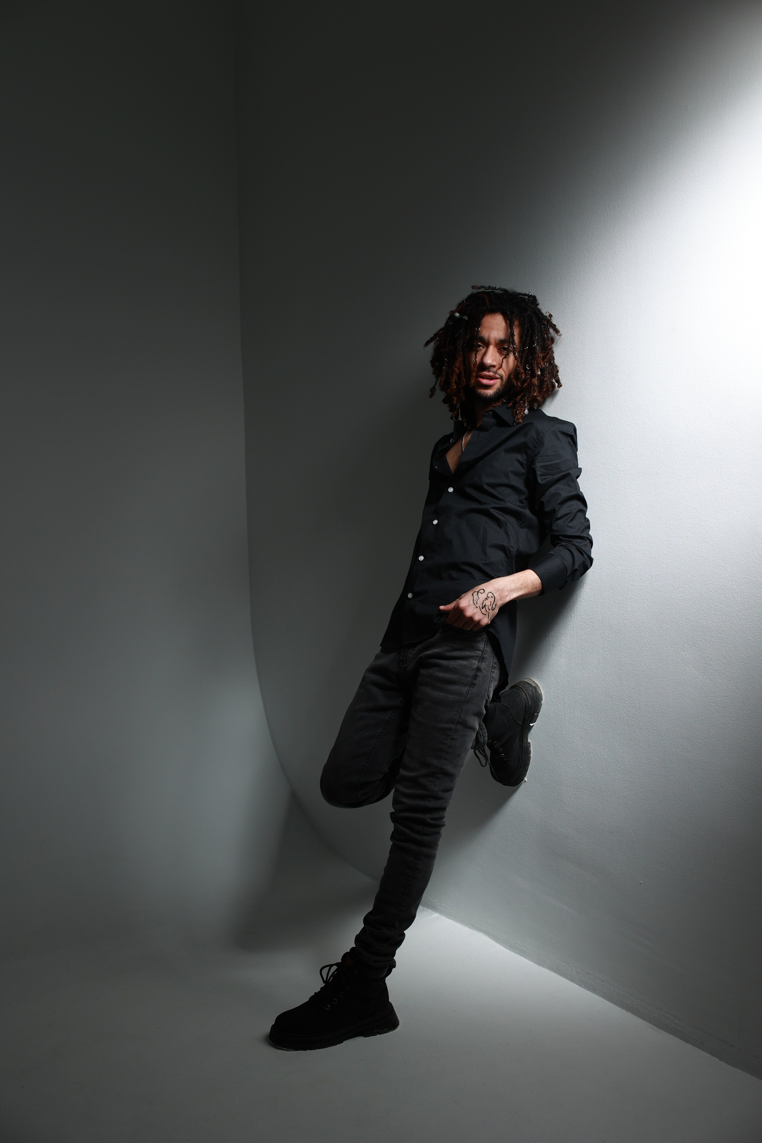 Темнокожий парень в черной одежде стоит у стены