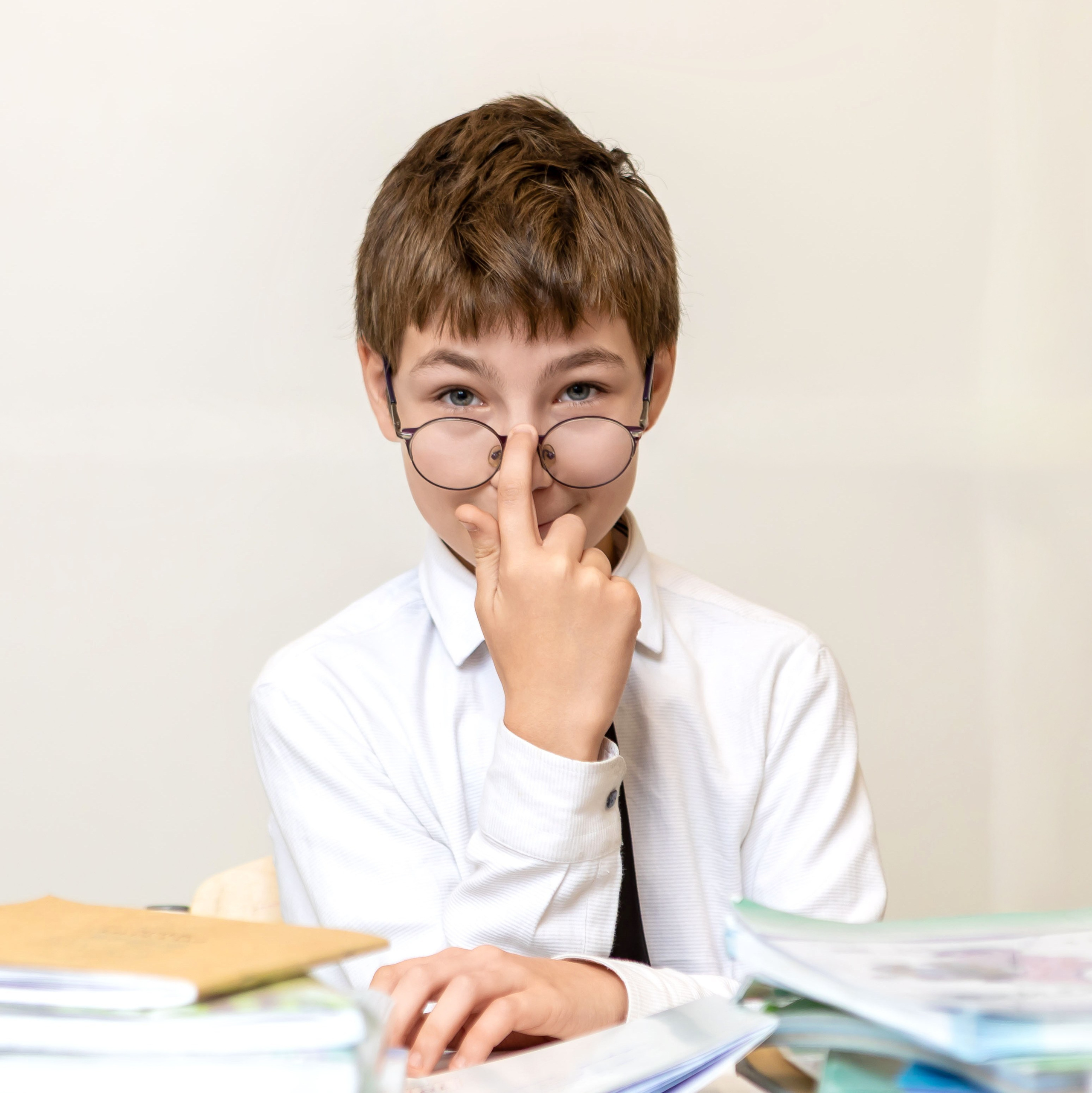 Мальчик с очками за партой, портрет школьника на светлом фоне