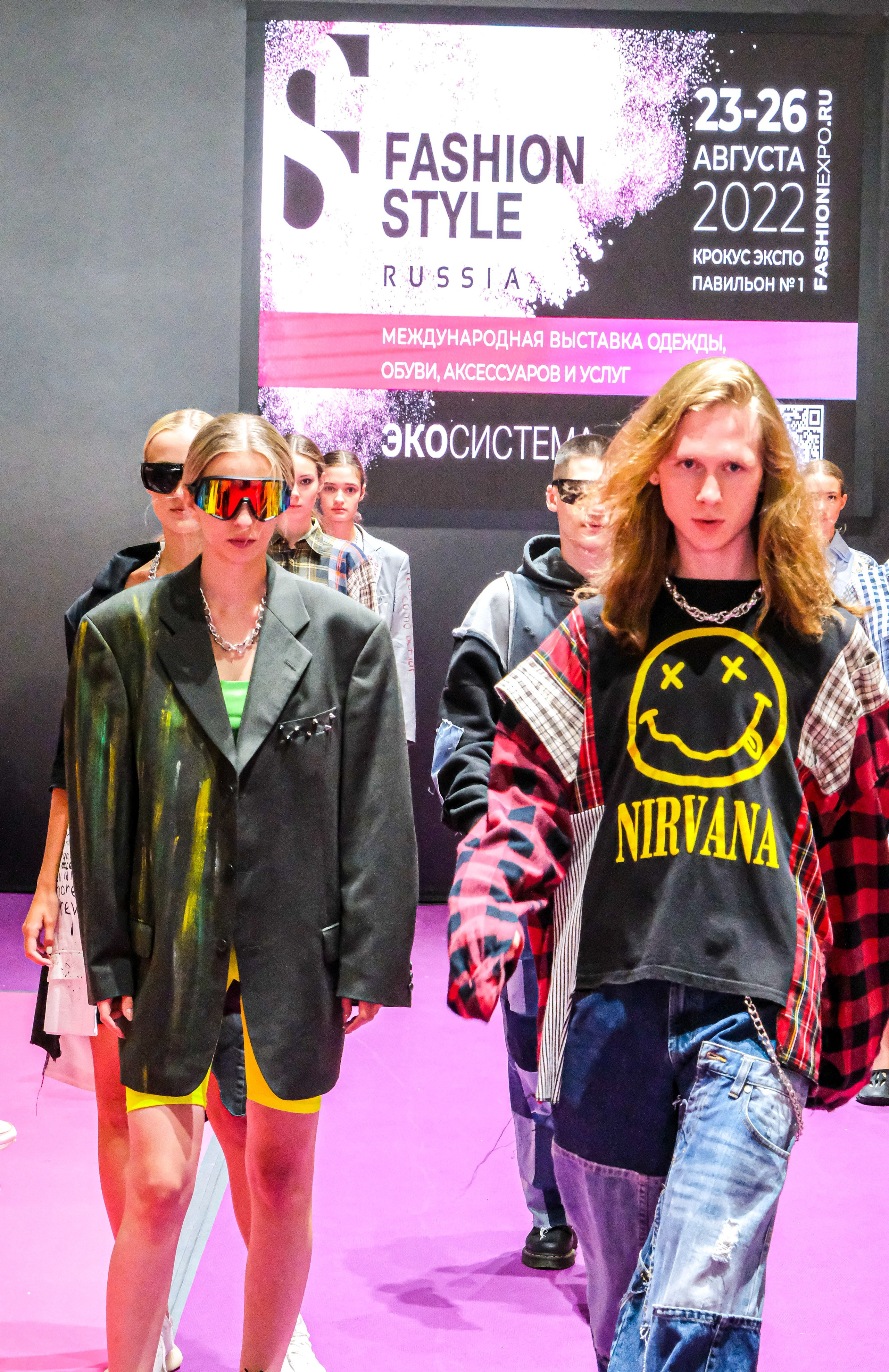  "Модели в ярких нарядах проходят по подиуму во время показа мод, освещенные яркими софитами и окруженные восторженными зрителями."