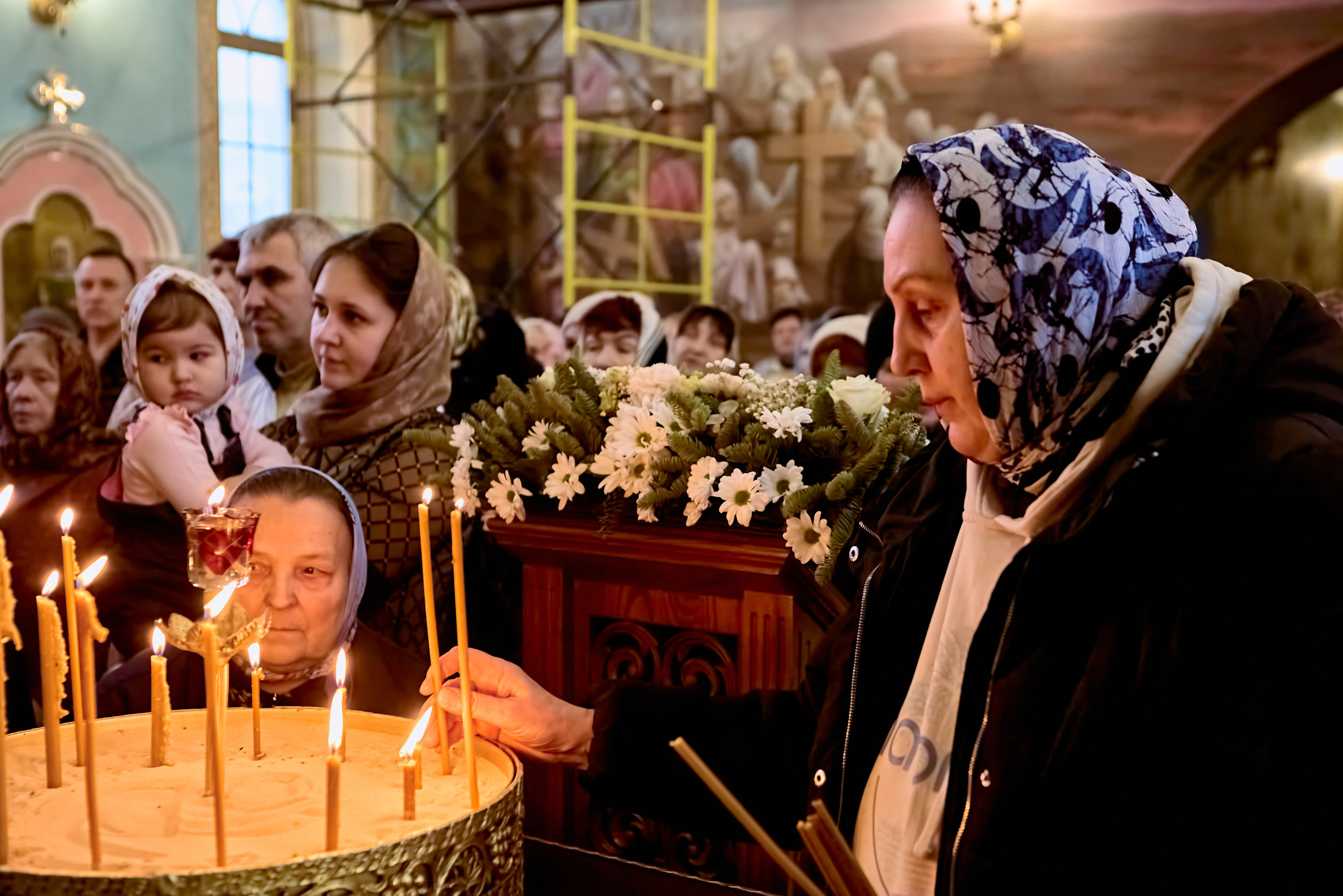 Женщина перед подсвечником зажигает свечу и ставит в подсвечник 