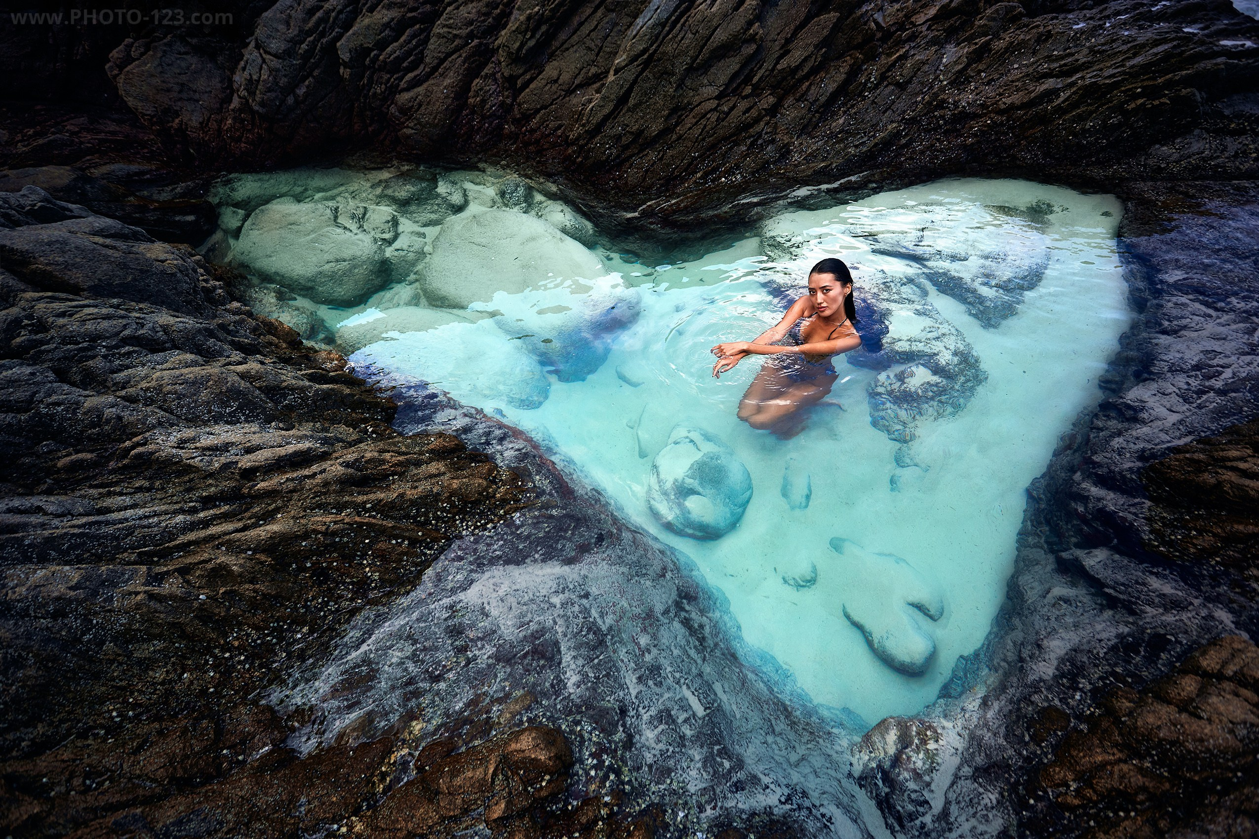 Cinematic photography of a model in a natural turquoise rock pool at a hidden gem location in Nha Trang.