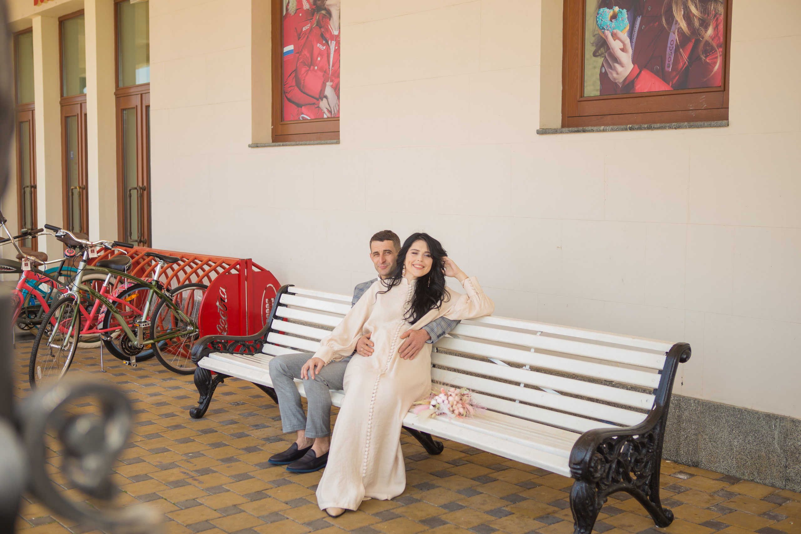 Жених и беременная невеста сидят на белой скамье