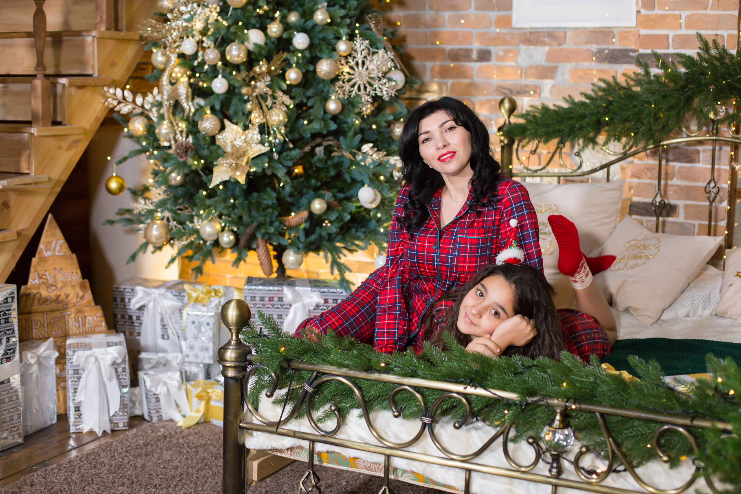 мама с дочкой в красных пижамах сидят на кровати в новогоднем интерьере