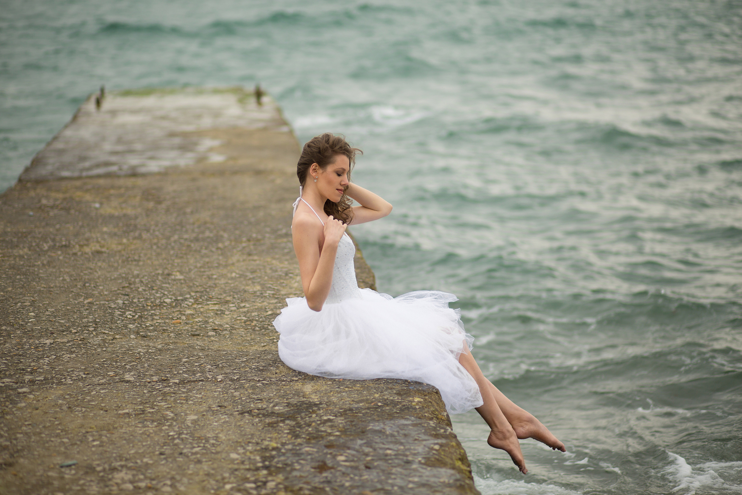 невеста сидит на пирсе на фоне волнующегося моря